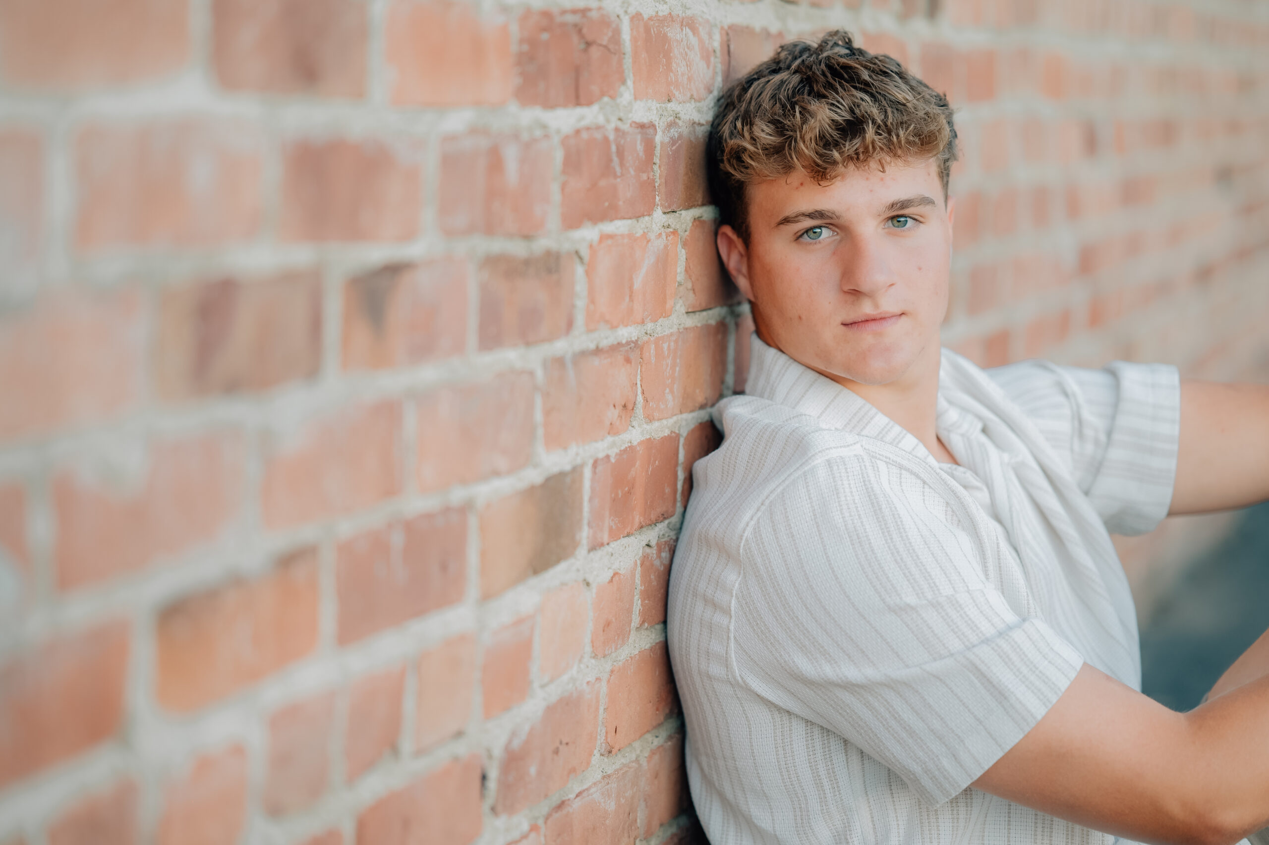 Graduate sits next to a brick wall while looking on at the camera.