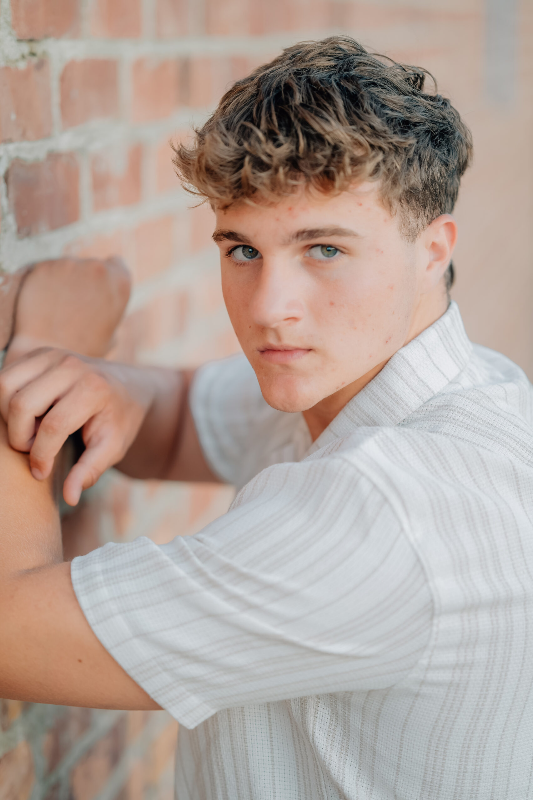 Graduate standing with hands folded on a brick wall while looking on at the camera.