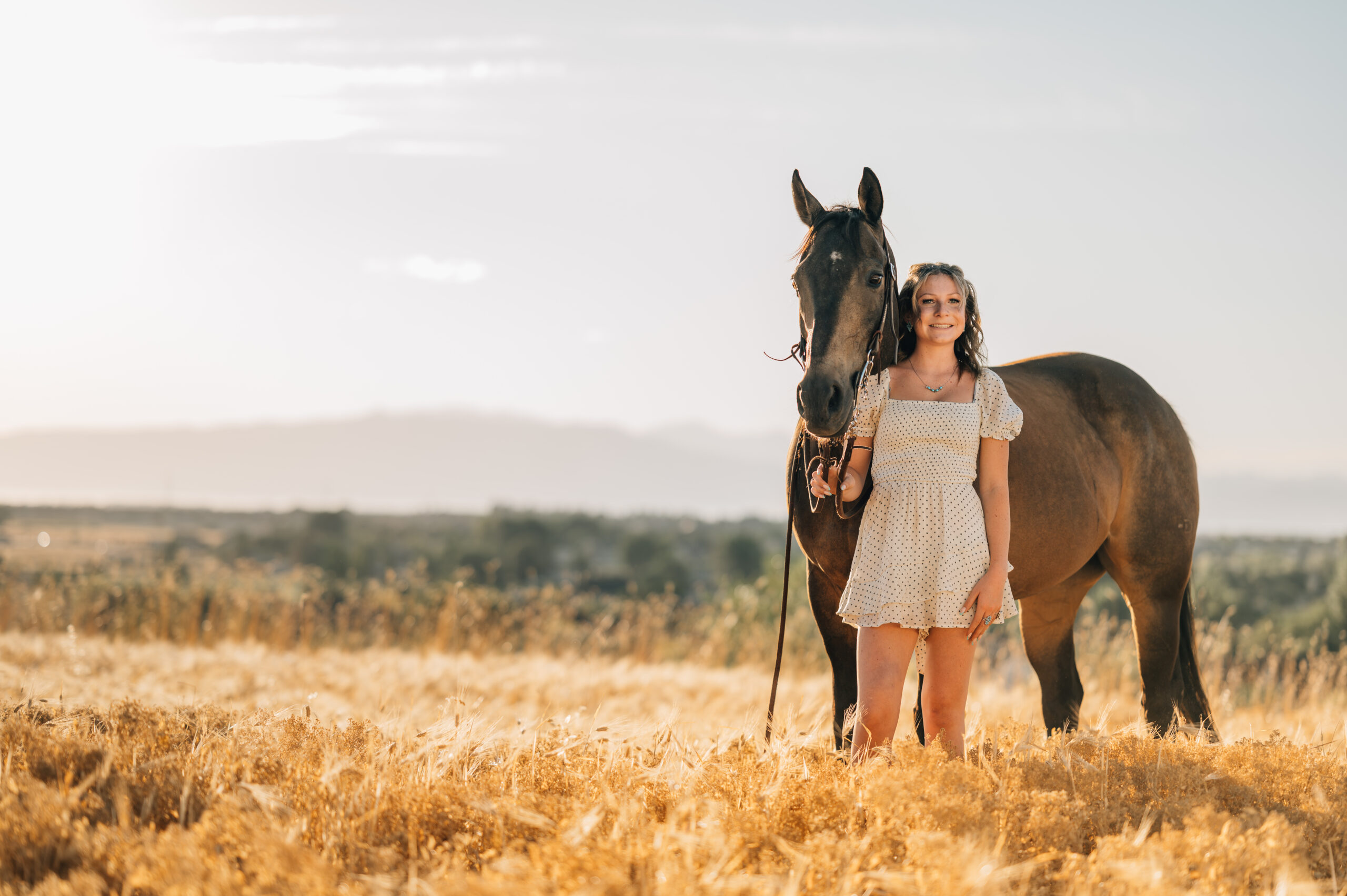 Just a girl with her horse. As the sun is setting a girl stands in front of her horse smiling on.
