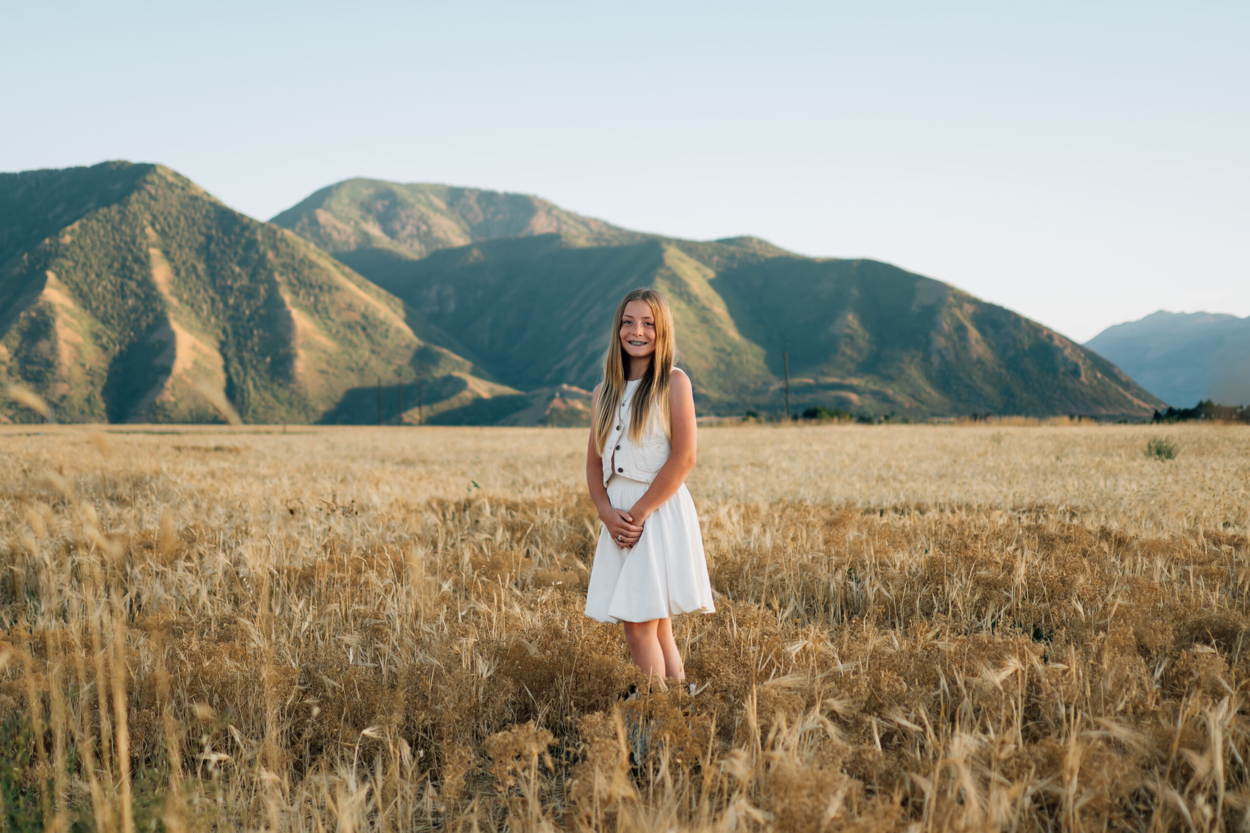 A girl stands with her hands relaxed in a clasp in front of her.