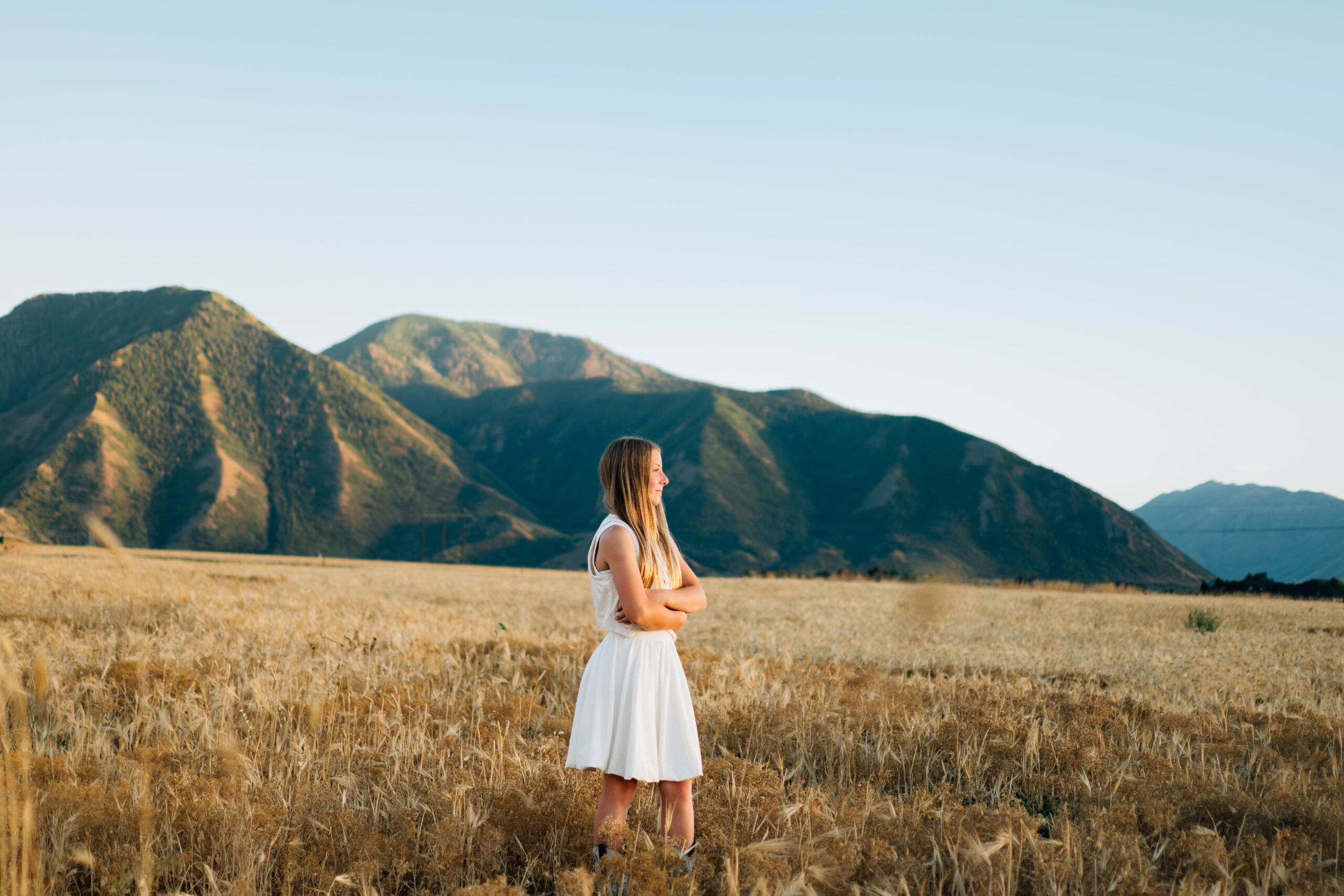 A girl stands with arms folded looking at the sunset. The picture is taken from the side.