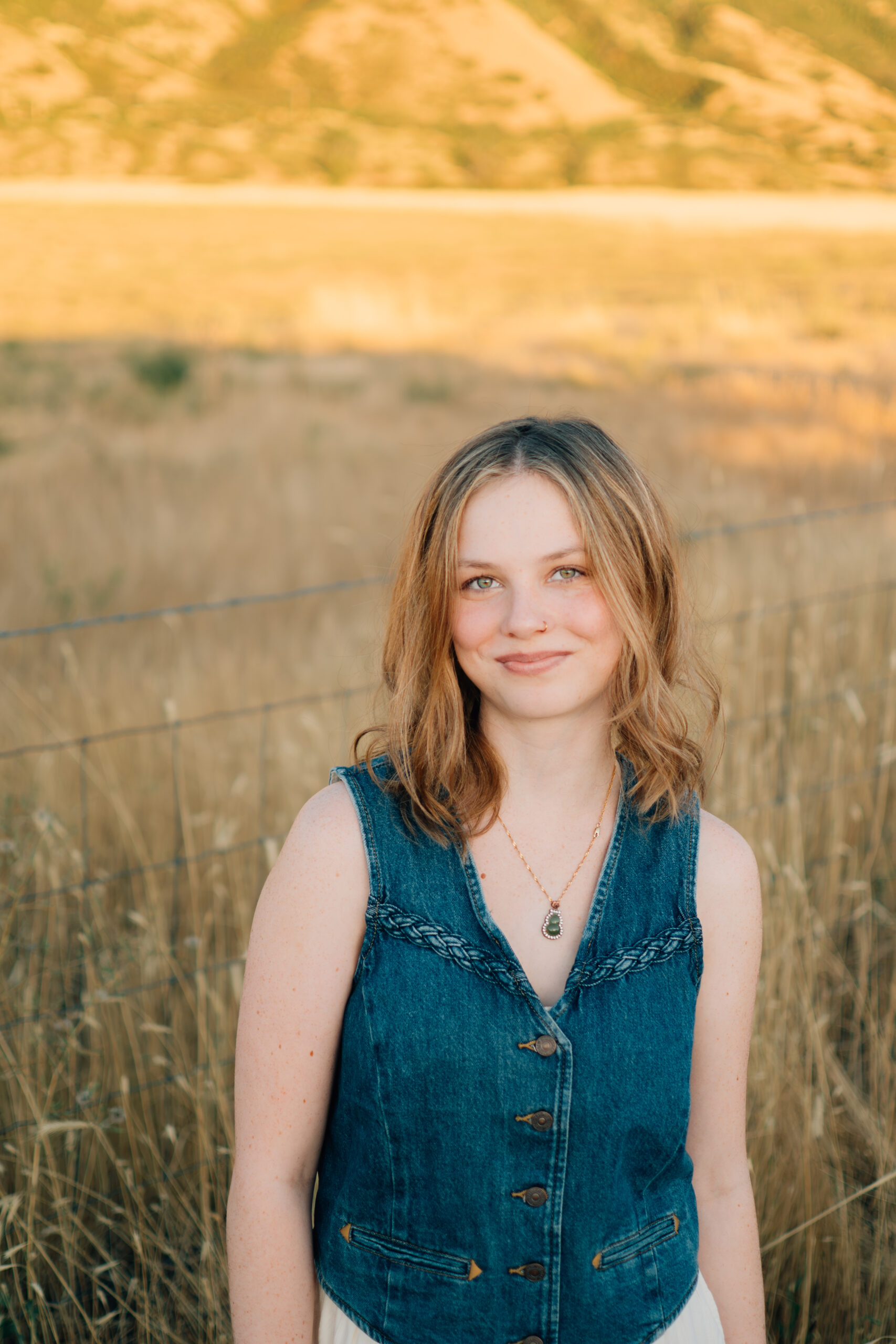A girl walks along a barbed wire fence through tall grass in the golden light.