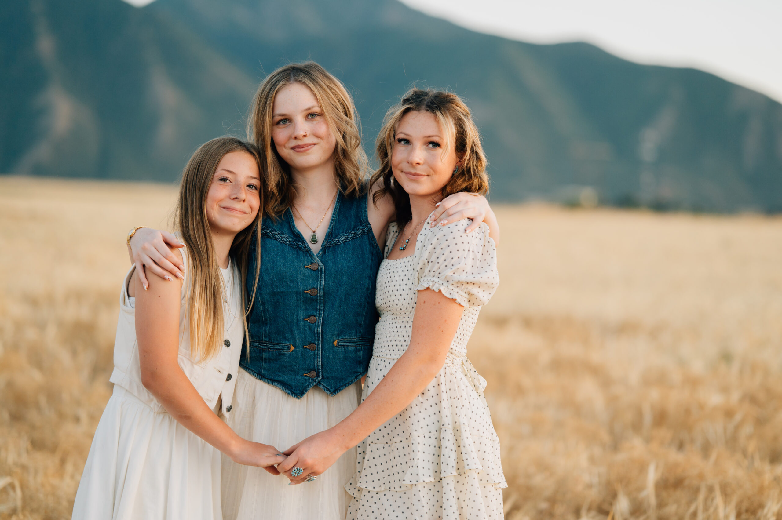 Sisters intertwined by holding holds while smiling for the camera in the golden light of the sunset.