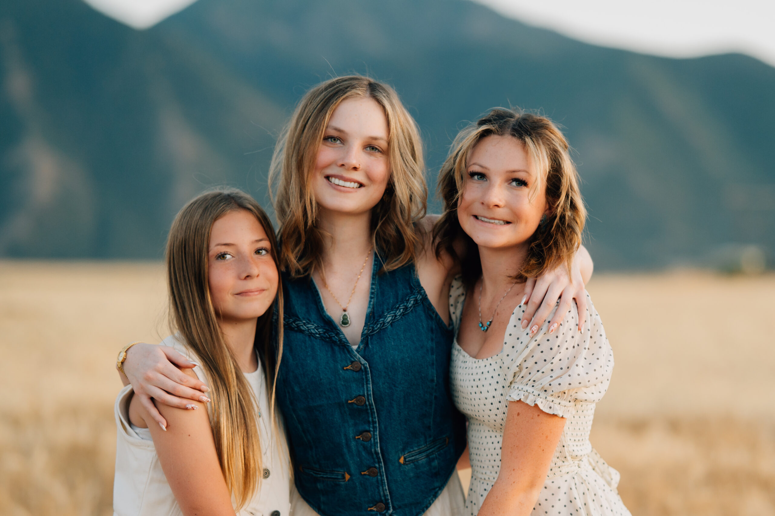 Sisters intertwined by holding holds while smiling for the camera in the golden light of the sunset.
