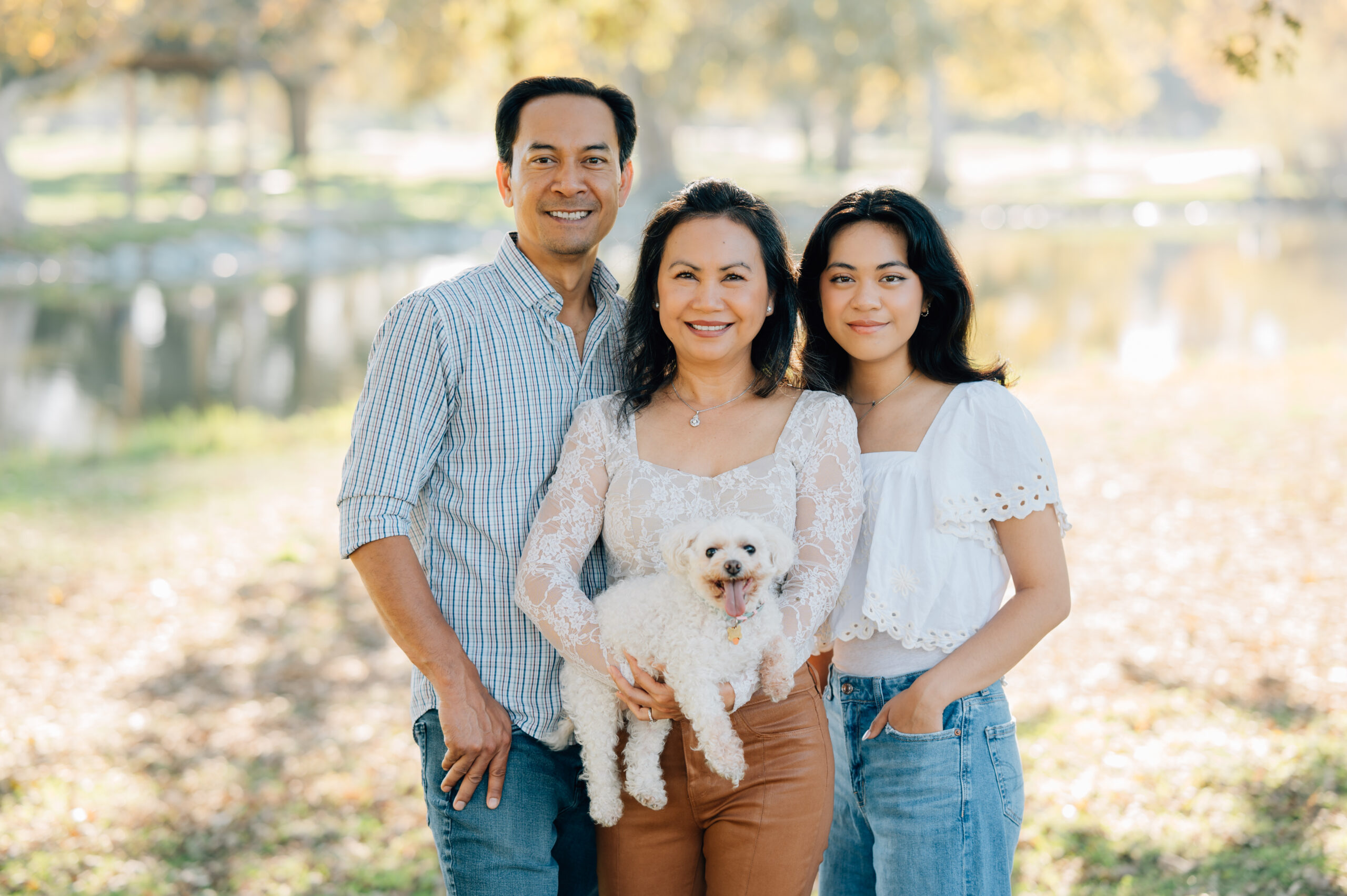 Family of three posing together by the lake at Oak Grove Park during a fall family photo session