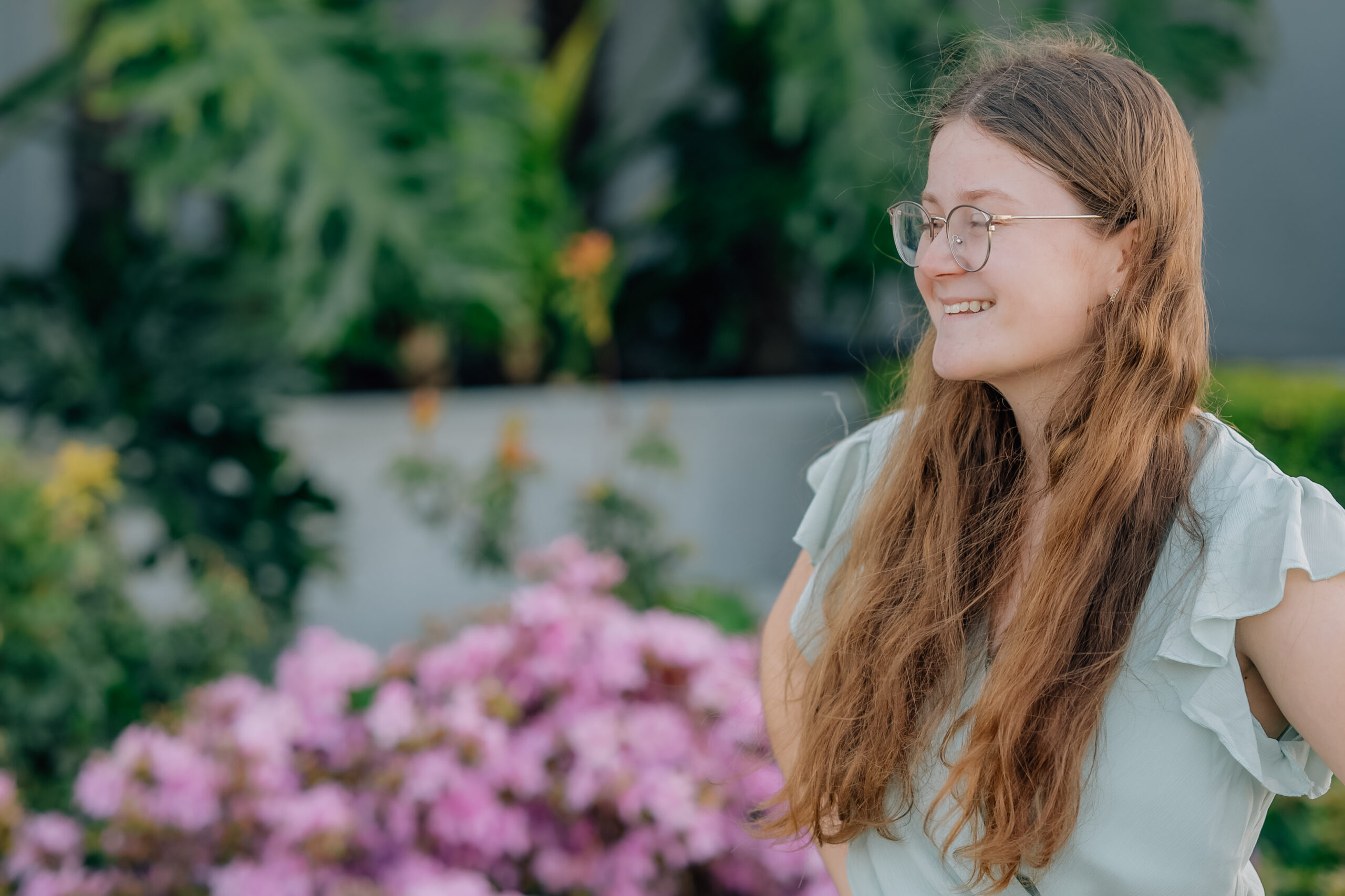 Senior girl in sage green dress smiling in front of pink flowers at the Oakland Temple grounds.