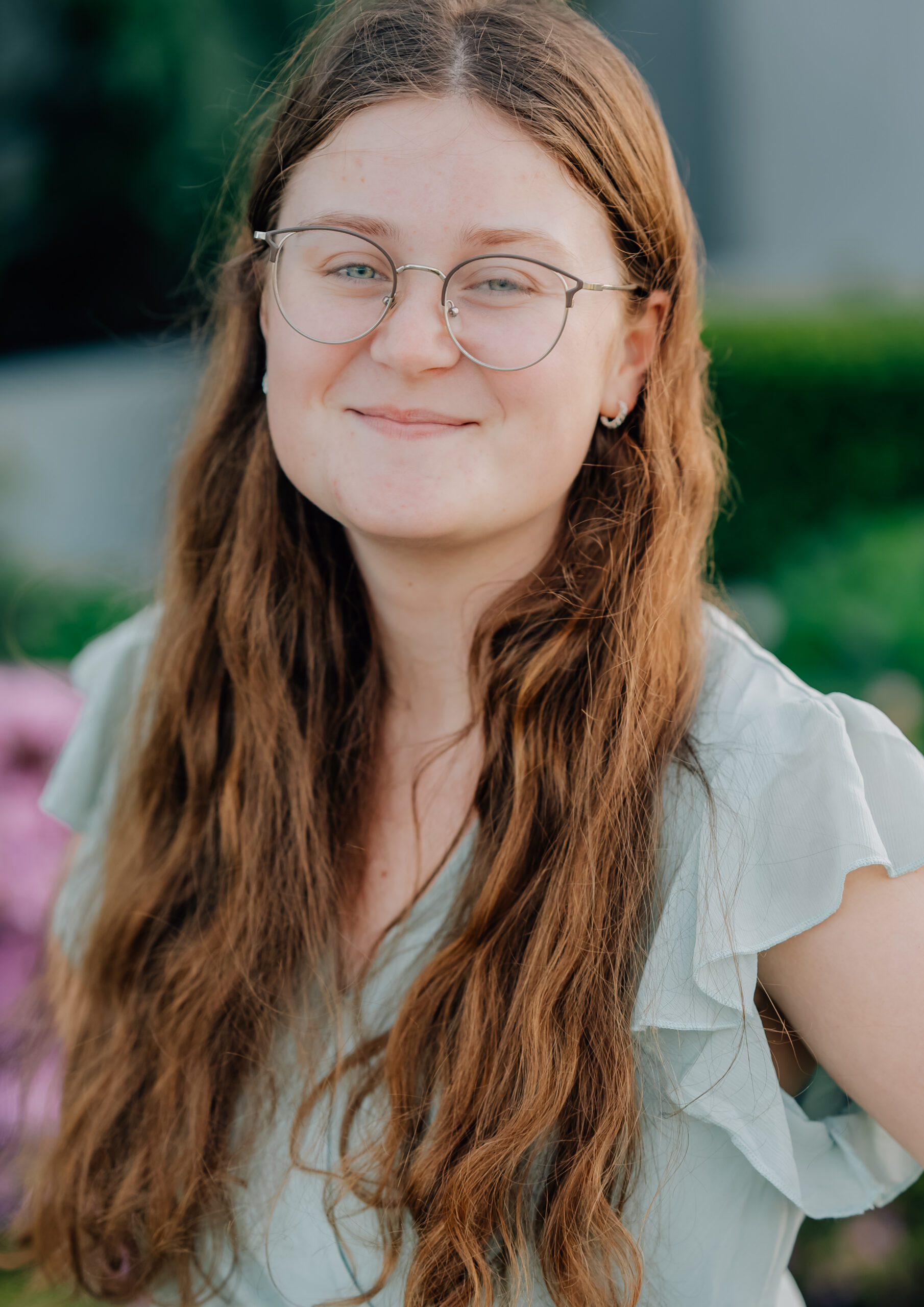 Senior girl in sage green dress smiling in front of pink flowers at the Oakland Temple grounds.