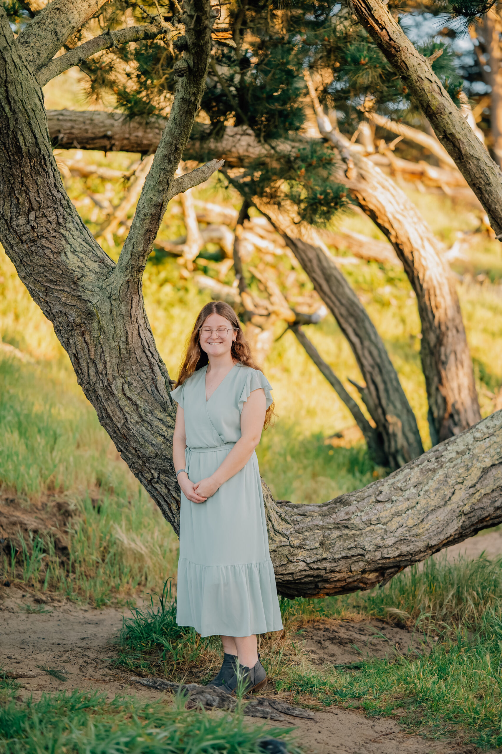 High school senior standing beside curved tree trunk during golden hour in Northern California.