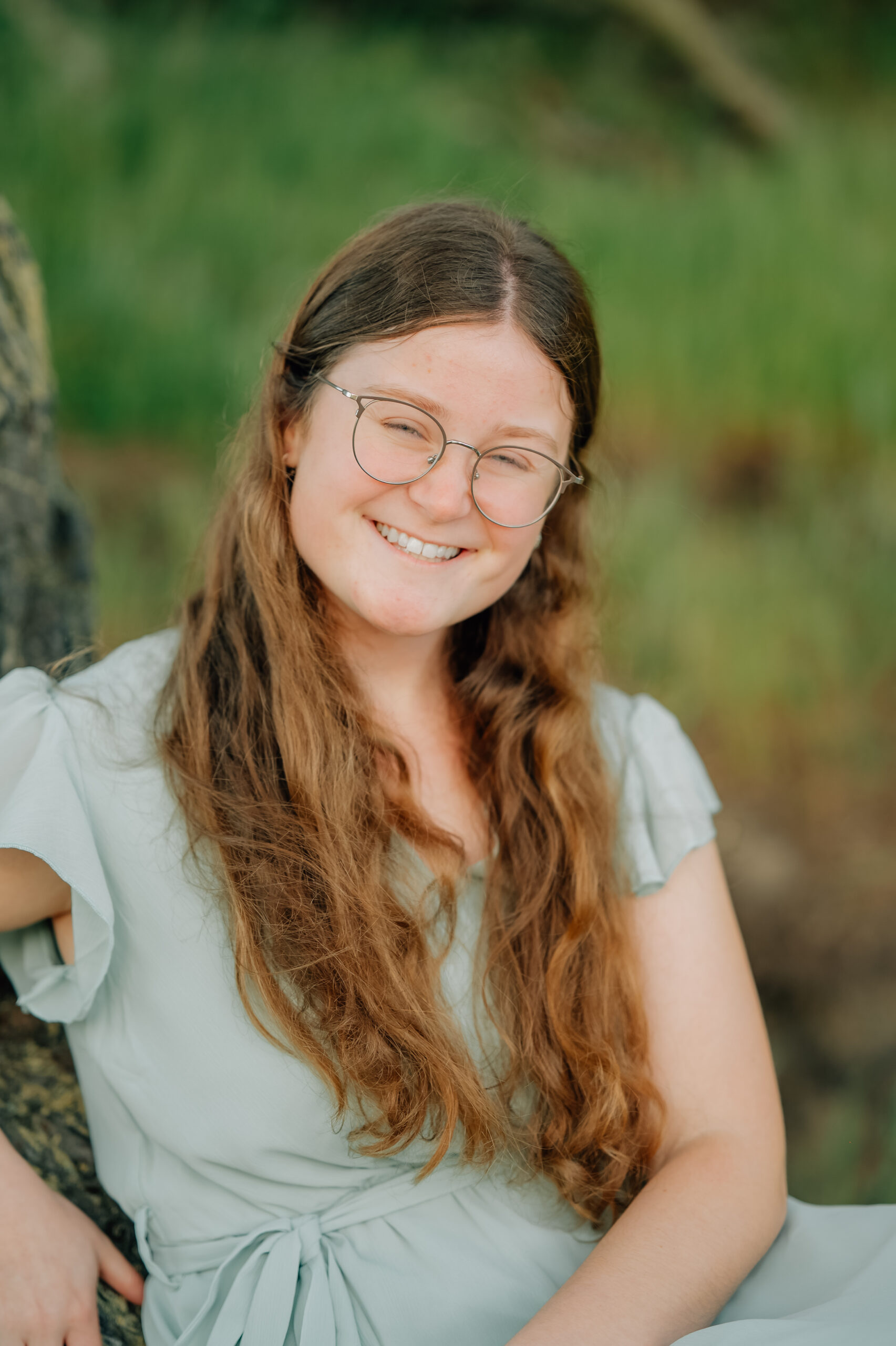 Full-length senior photo in sage green dress surrounded by trees and soft evening light.