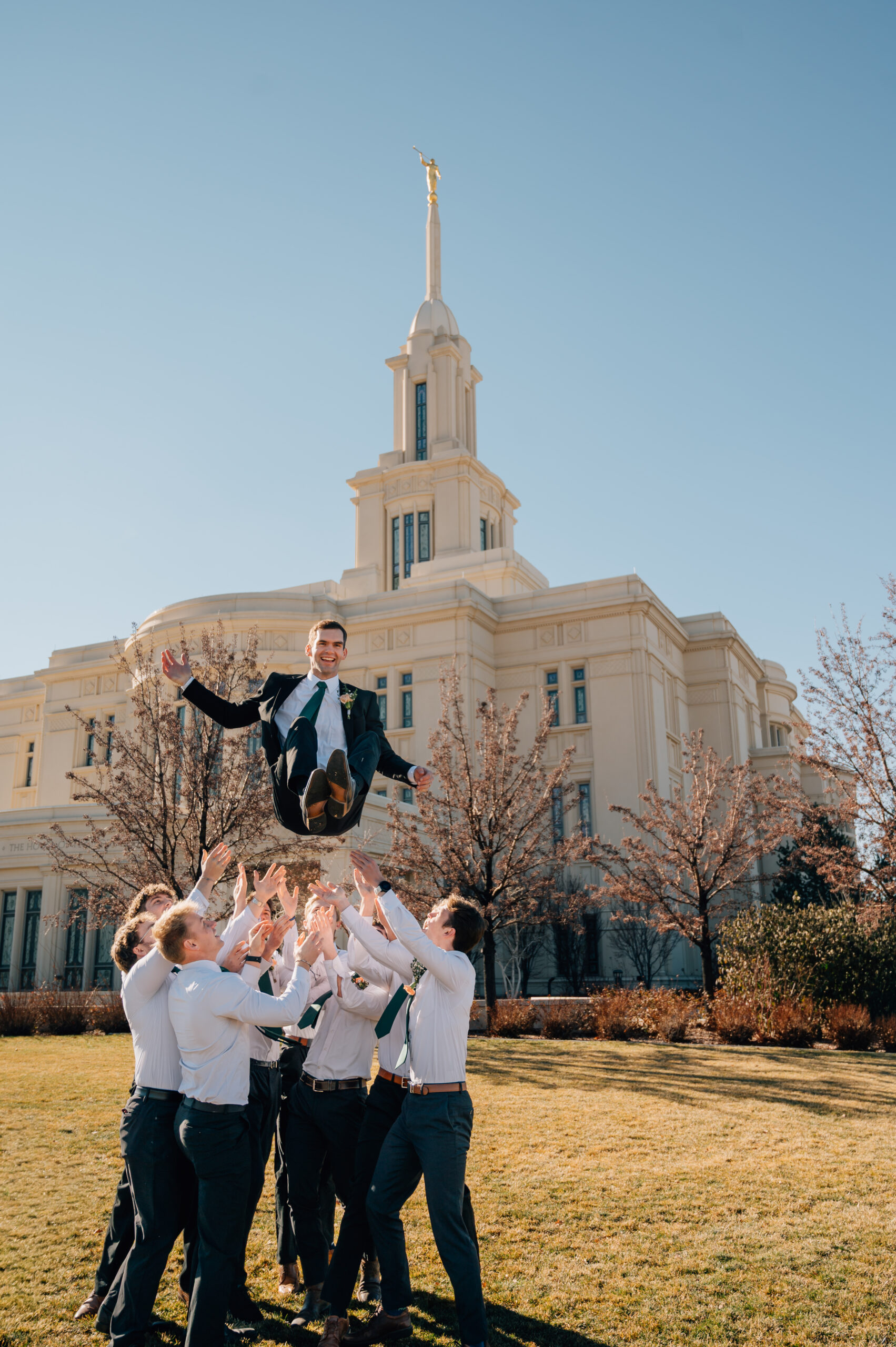 Groomsmen throwing the groom in the air outside the Payson Utah Temple