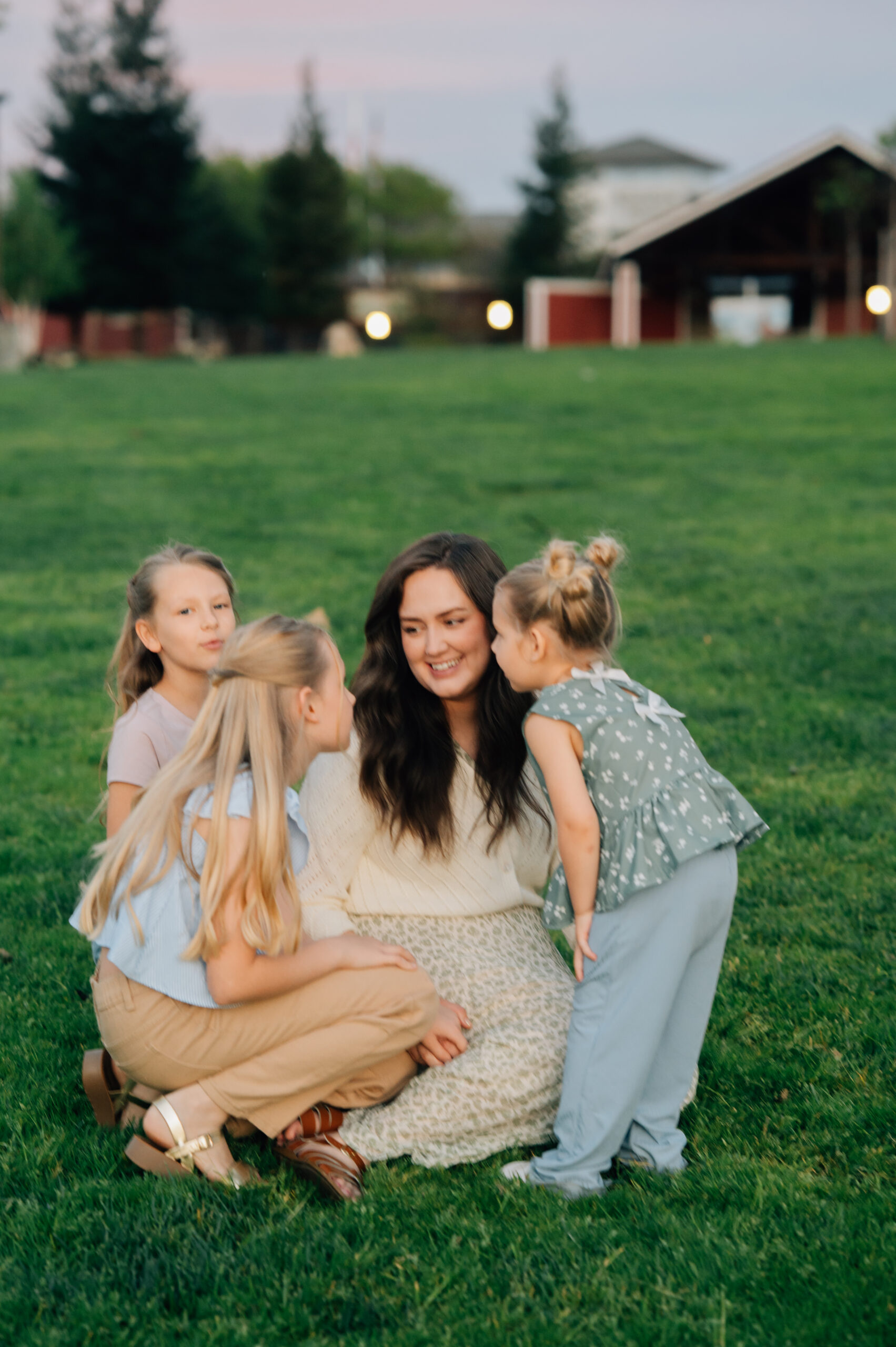 Mom sitting in the grass while her daughters gather around her during sunset family photos