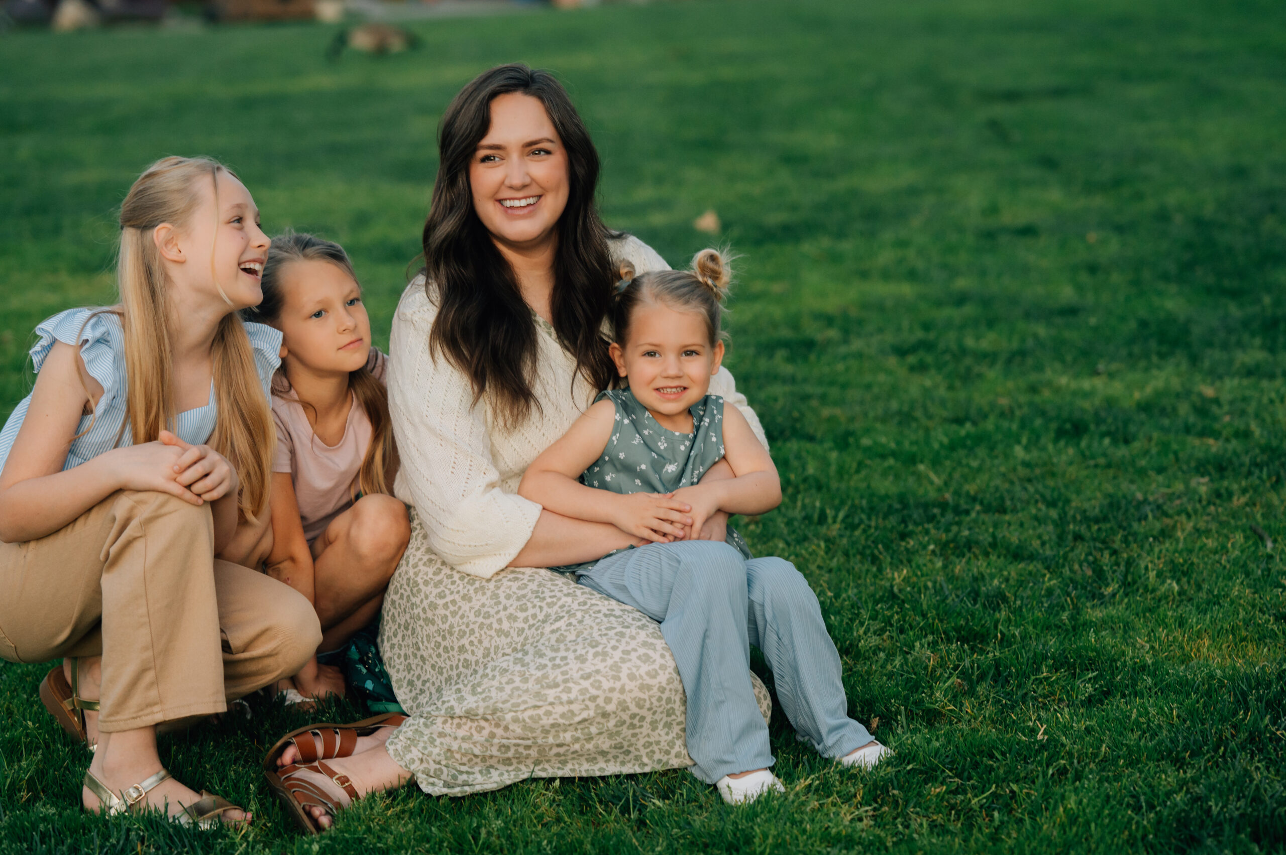 Mom sitting in the grass while her daughters gather around her during sunset family photos