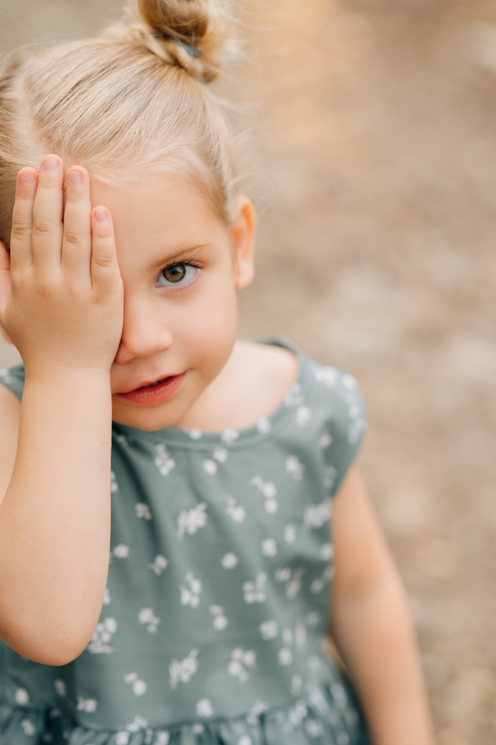 Close-up portrait of a young girl covering one eye during a playful outdoor family session