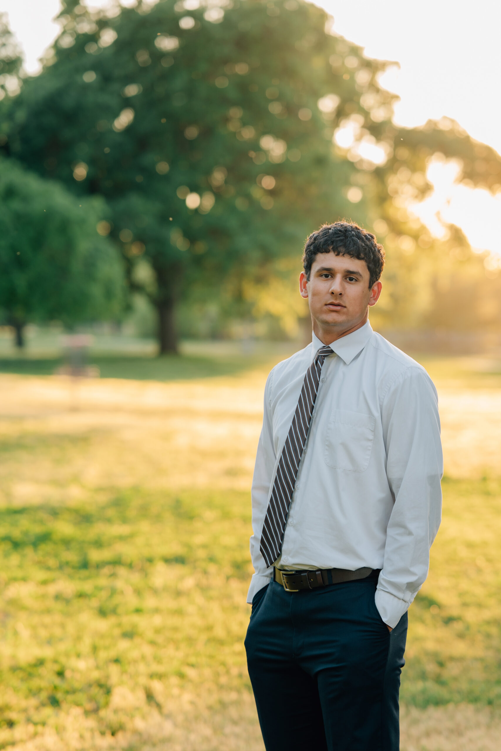 Senior boy standing at golden hour in front of trees at Shumway Oak Grove Park in Stockton 