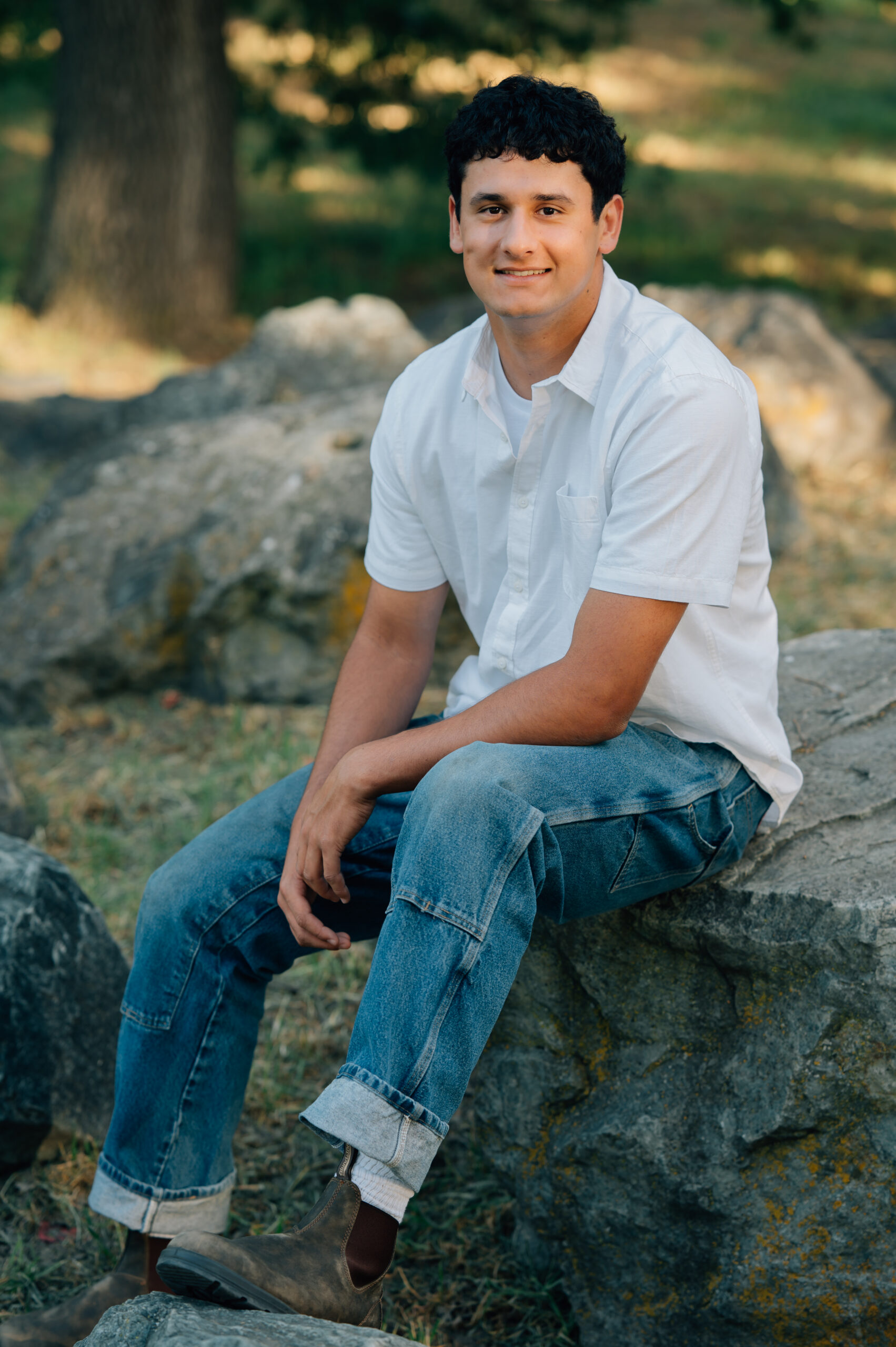 Senior boy at Shumway Oak Grove Park in Stockton sitting on a rock and smiling
