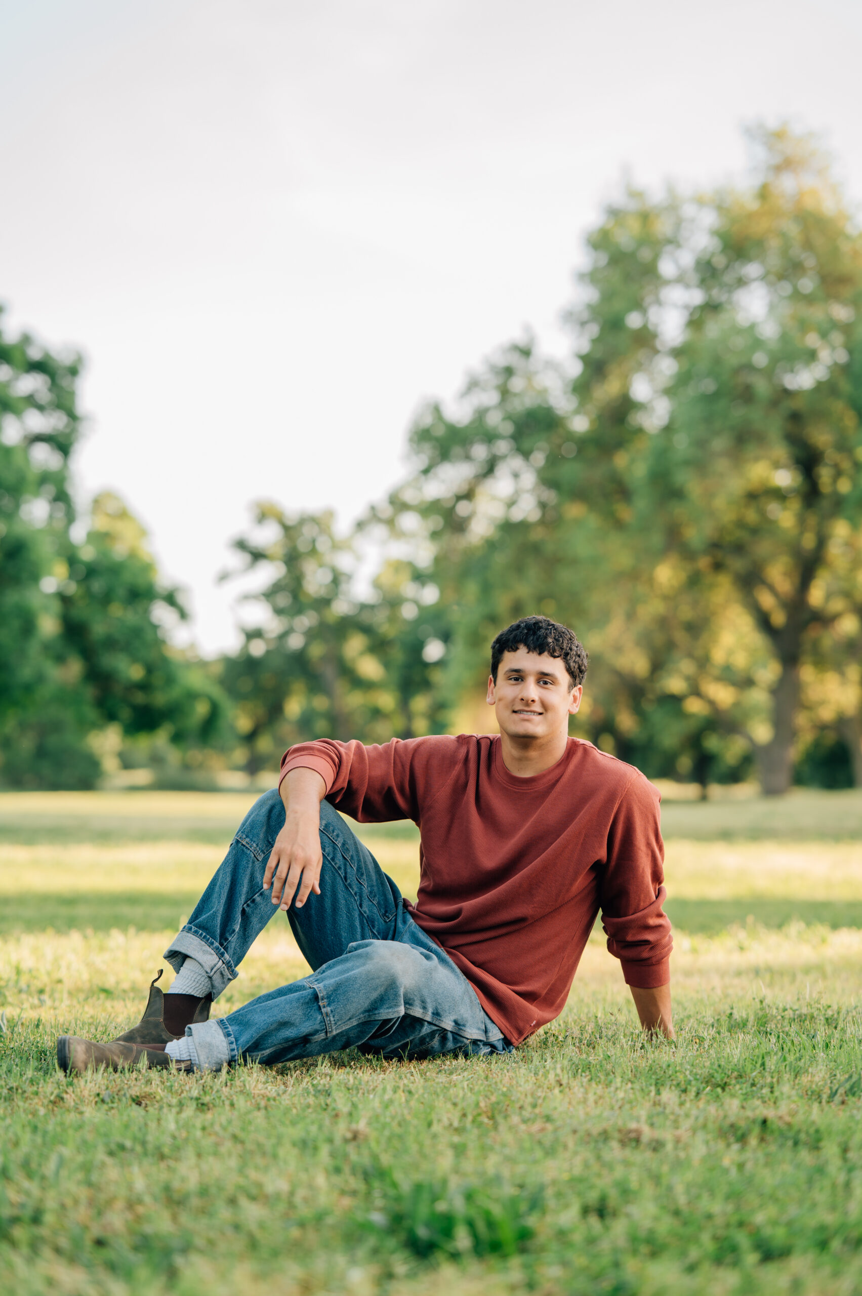 Senior boy sitting in front of trees at Shumway Oak Grove Park in Stockton 
