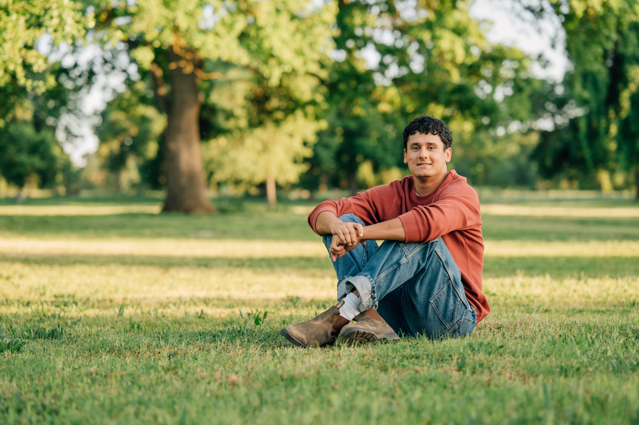 Senior boy sitting in front of trees at Shumway Oak Grove Park in Stockton 