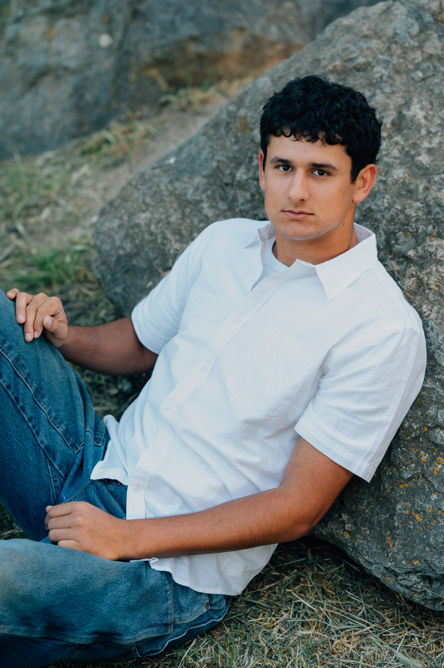 Senior boy at Shumway Oak Grove Park in Stockton sitting on a rock and smiling