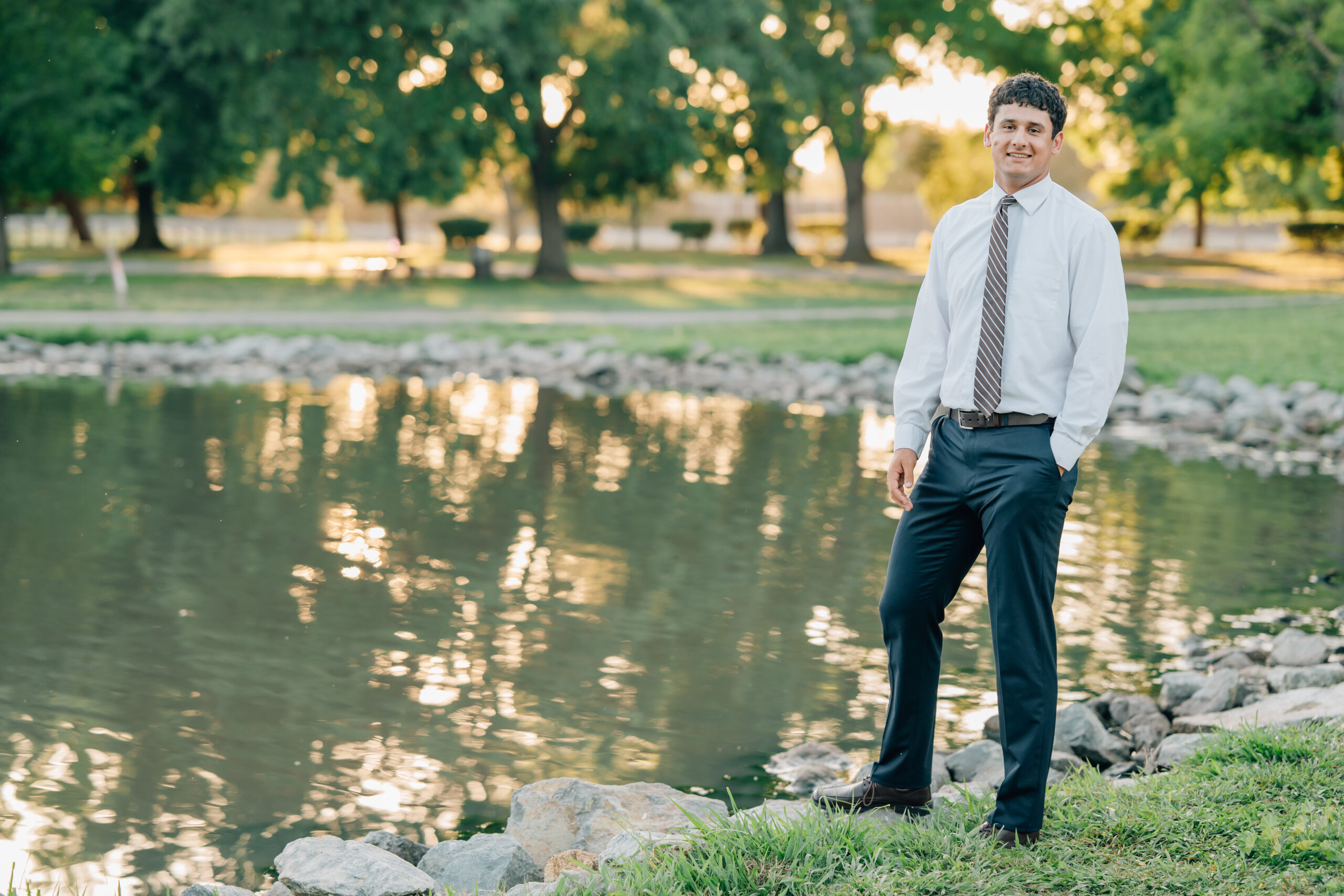 Senior boy standing by a lake at Shumway Oak Grove Park in Stockton during golden hour