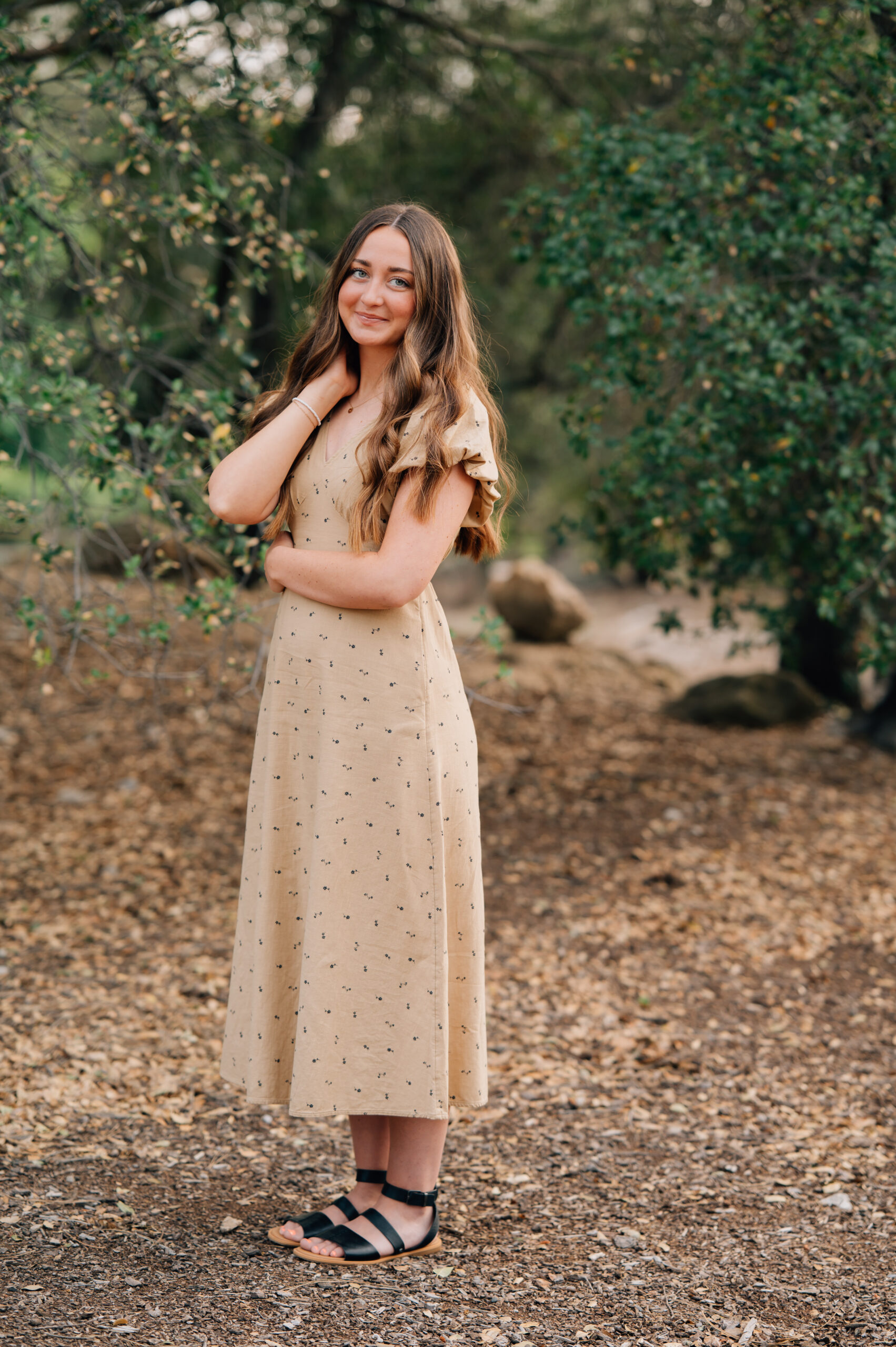 Senior girl posing naturally in tan dress surrounded by trees at Quarry Park