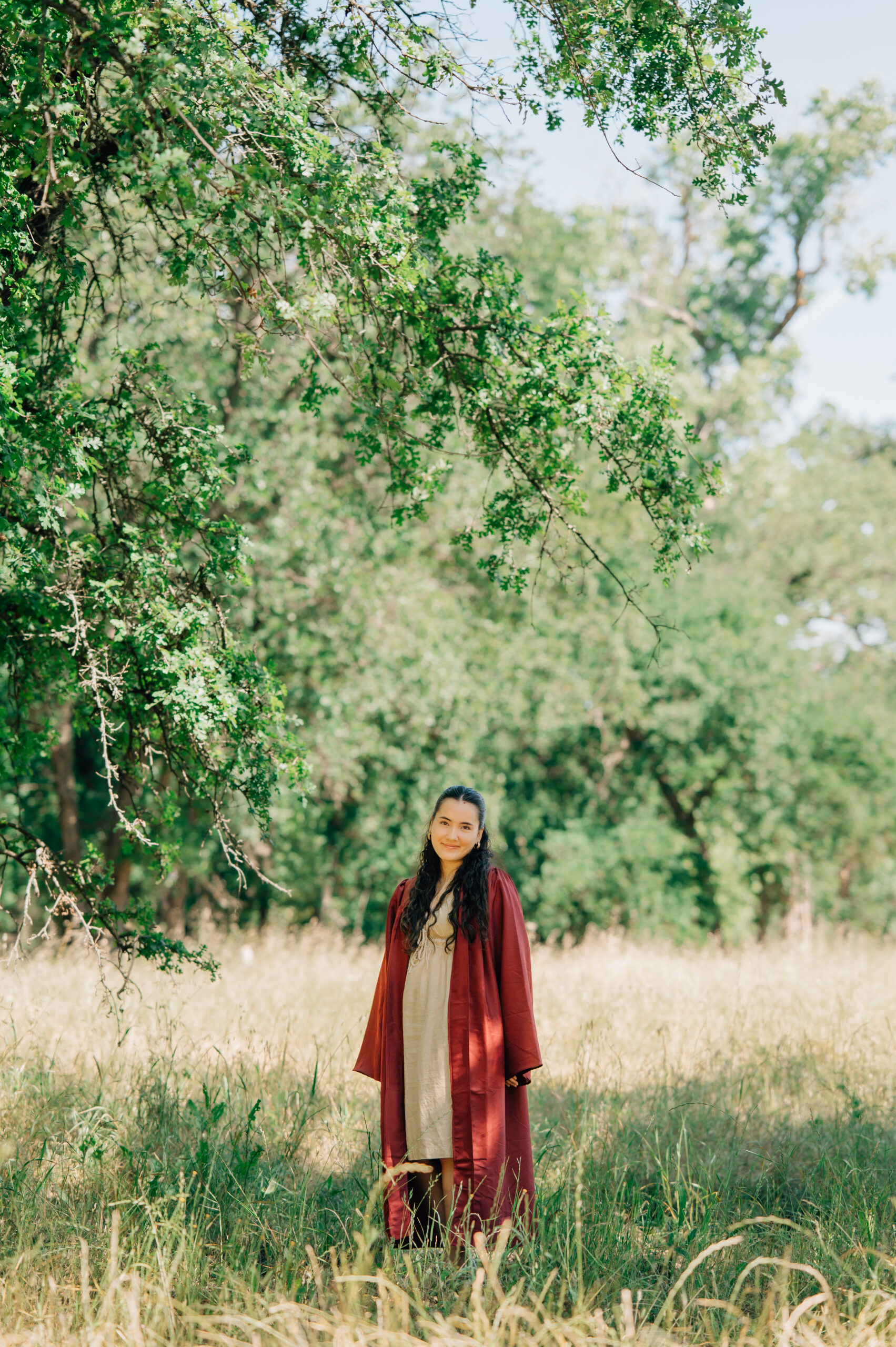 Senior graduate walking through field with cap and gown during graduation portraits