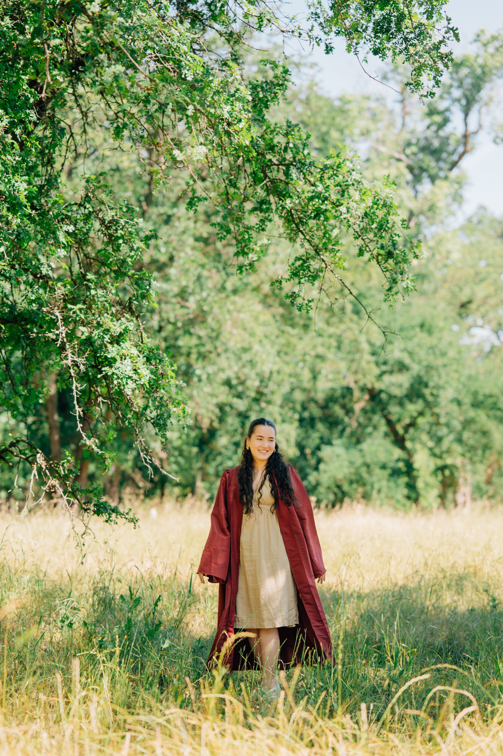 Senior graduate walking through field with cap and gown during graduation portraits