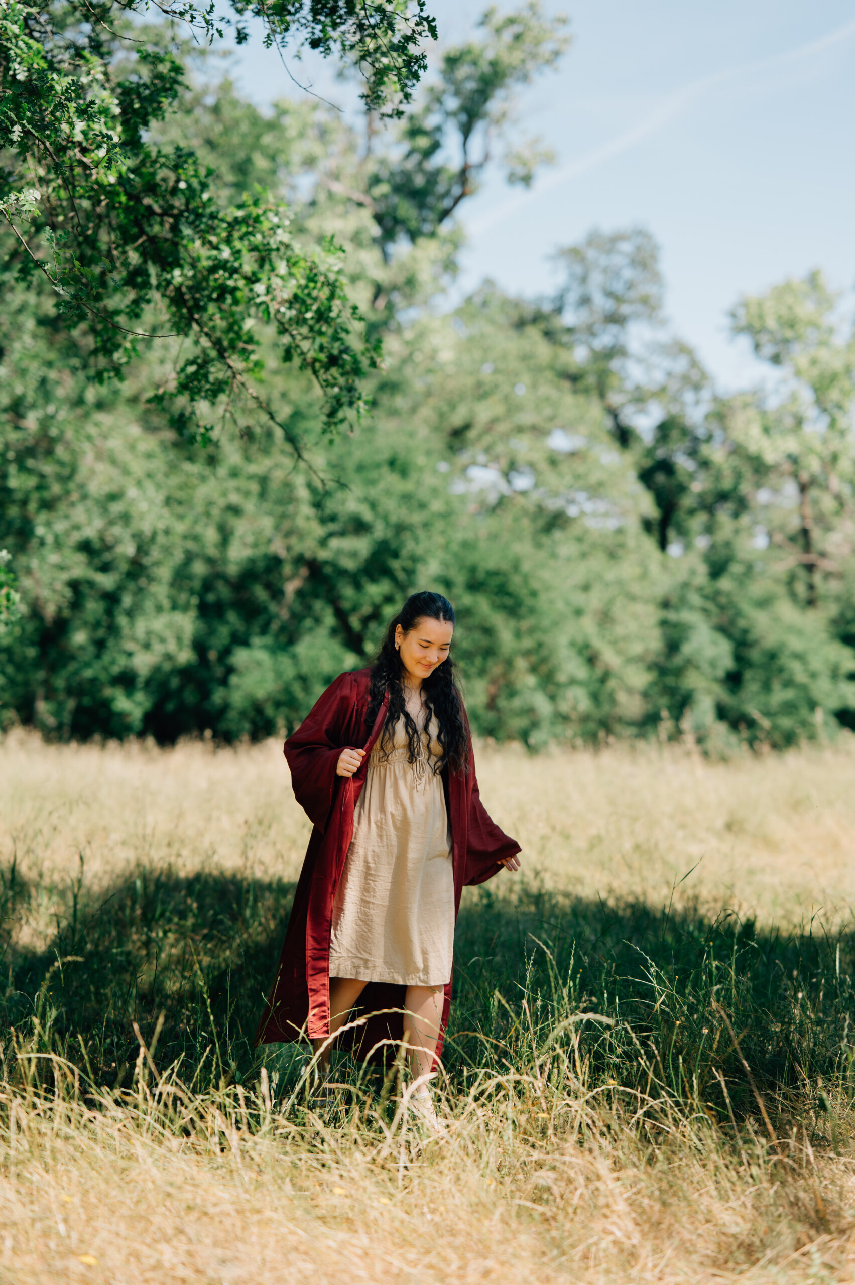 Senior graduate walking through field with cap and gown during graduation portraits