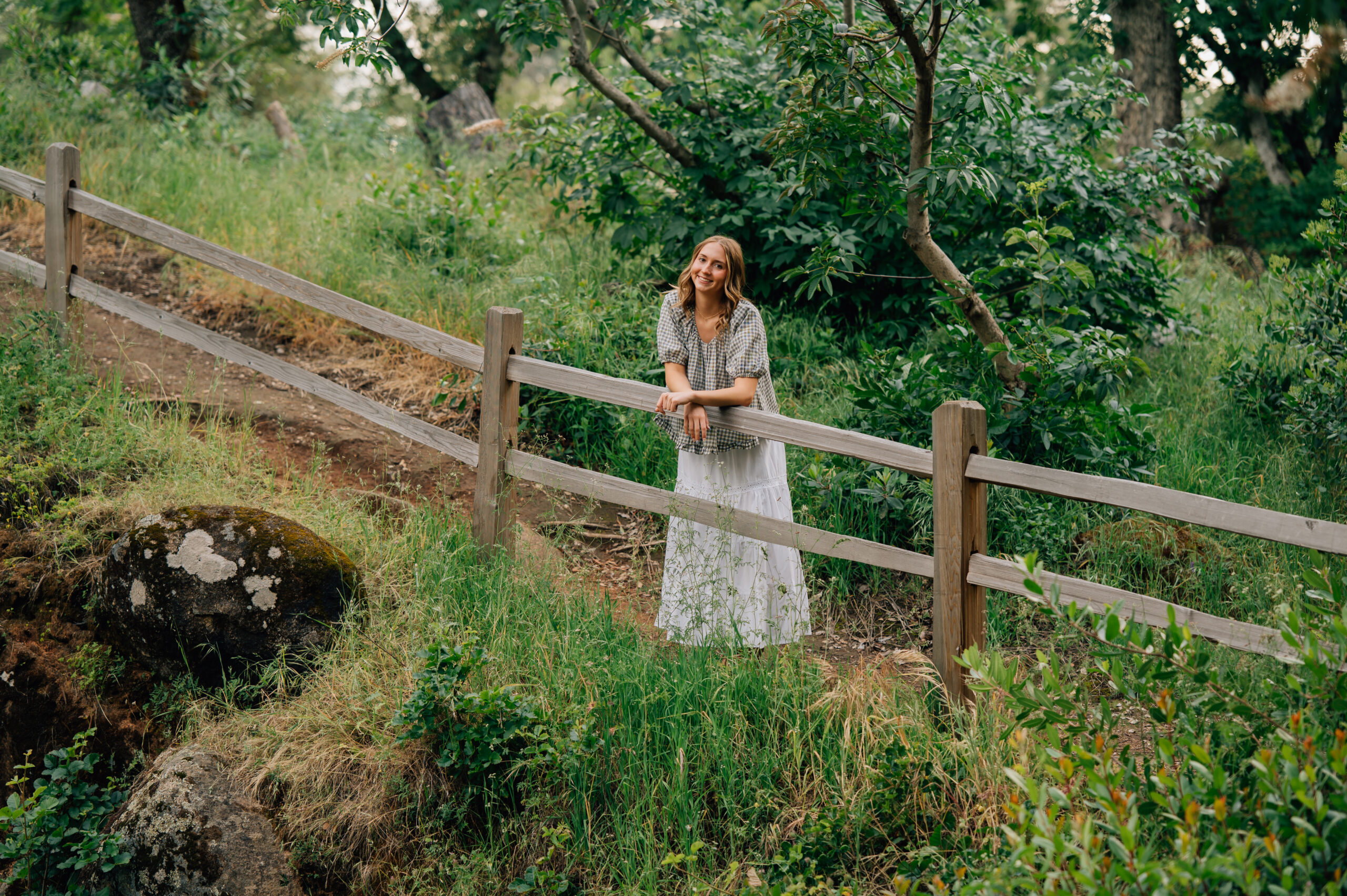 High school senior leaning on a wooden fence surrounded by lush greenery during a Penryn senior photo session.