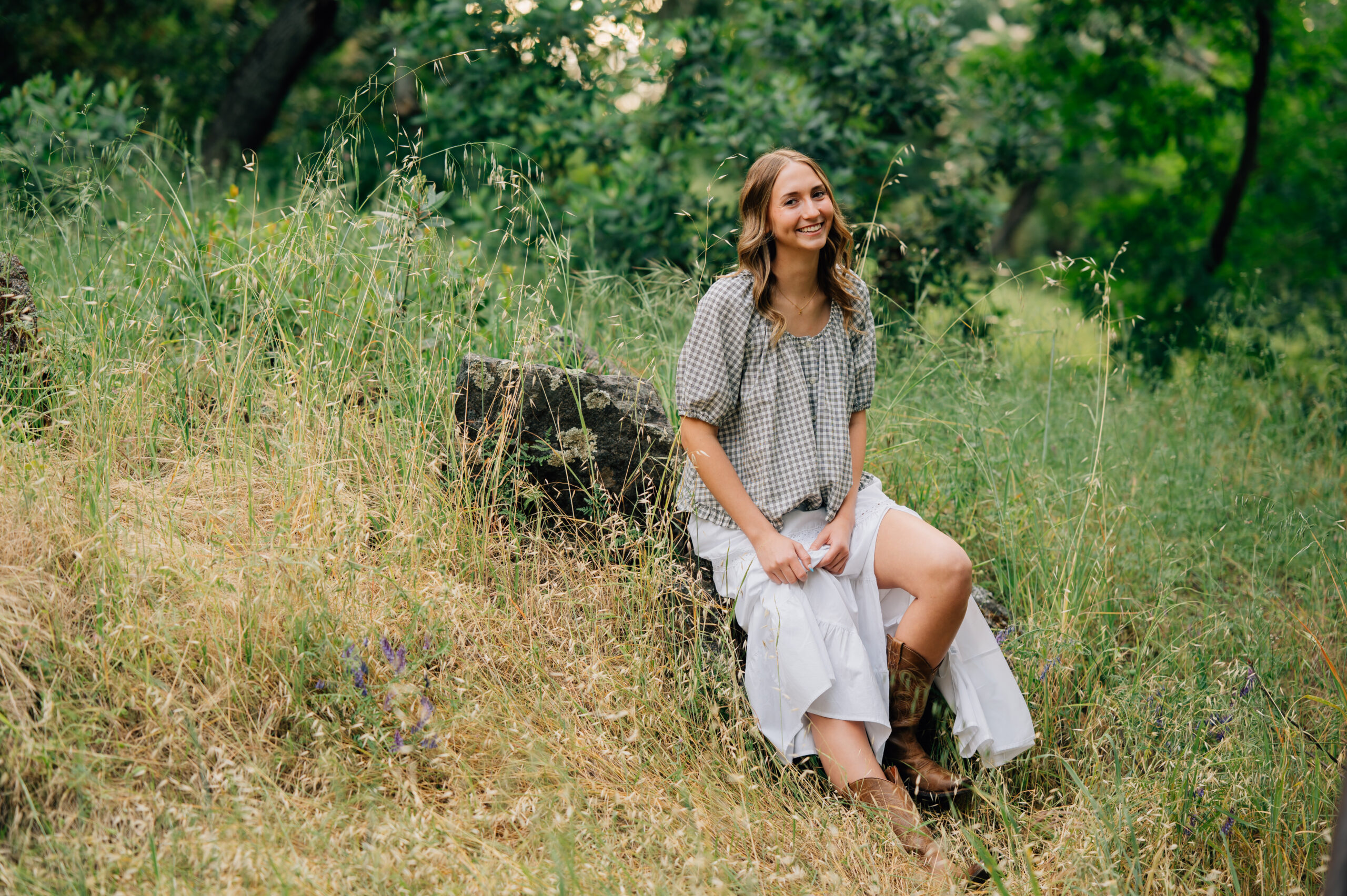 Senior girl in white skirt and cowboy boots sitting on a boulder at sunset in Northern California.