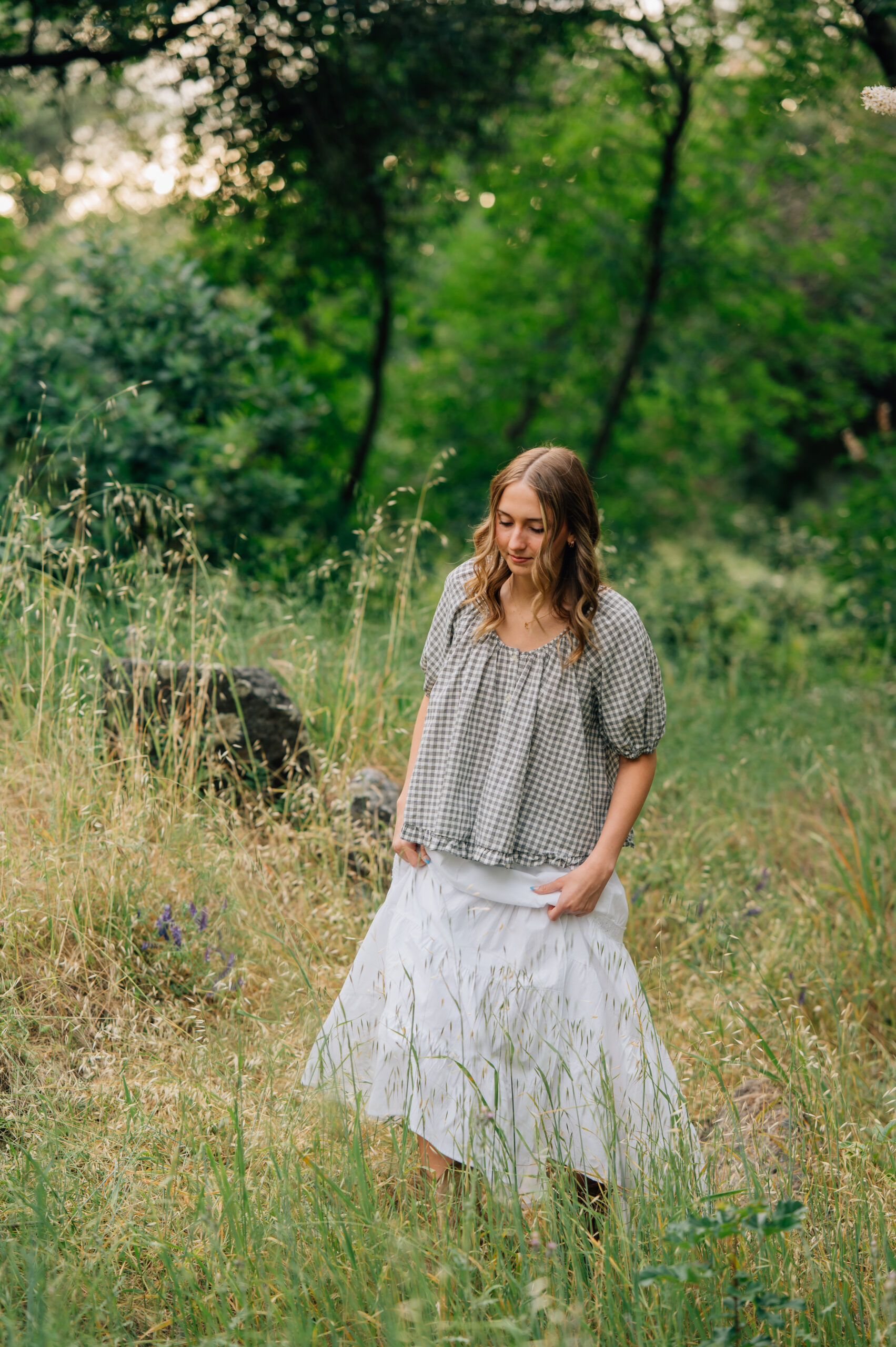 High school senior walking through tall grass in a flowing white skirt during golden hour at Griffith Quarry Park.