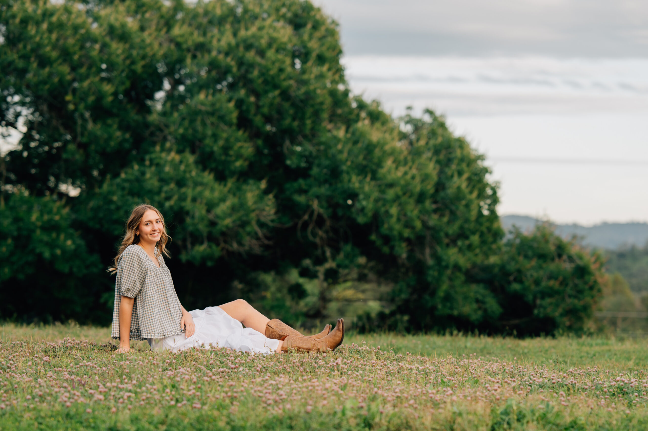 Natural senior portrait of graduate sitting in wild grass and smiling during a golden hour session in Penryn.