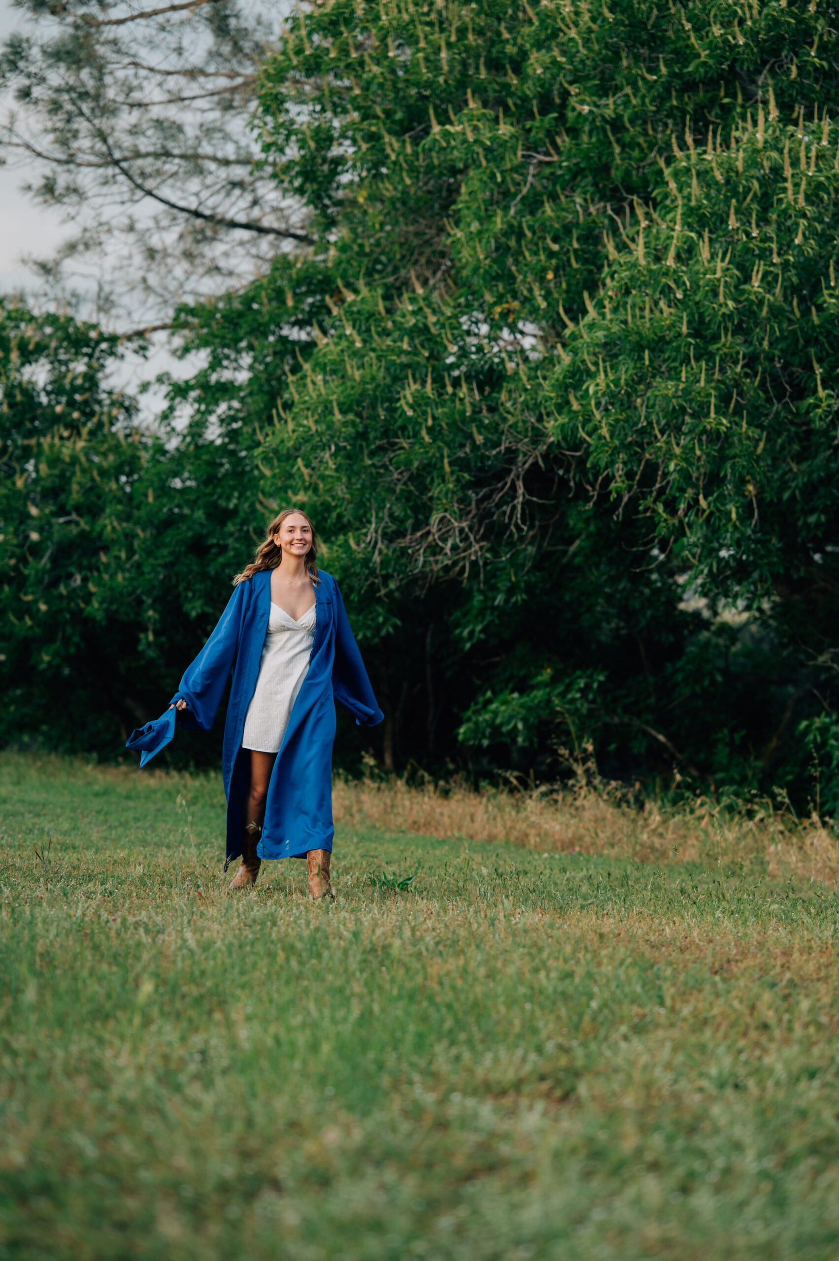 High school graduate wearing blue cap and gown surrounded by greenery and walking during outdoor senior portraits in Penryn.