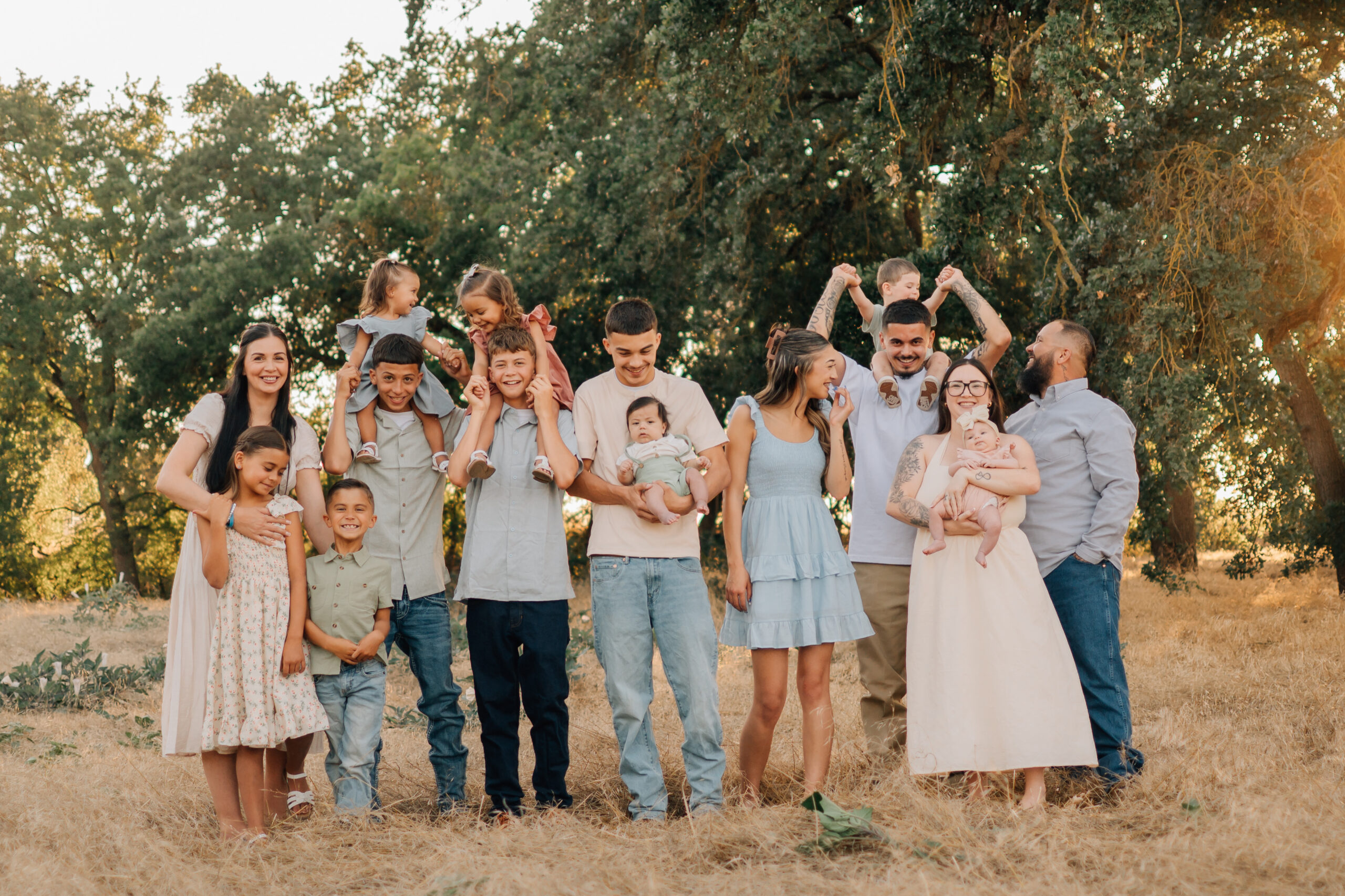 Large extended family laughing and interacting together in a sunlit field at Oak Grove Park in Ripon.