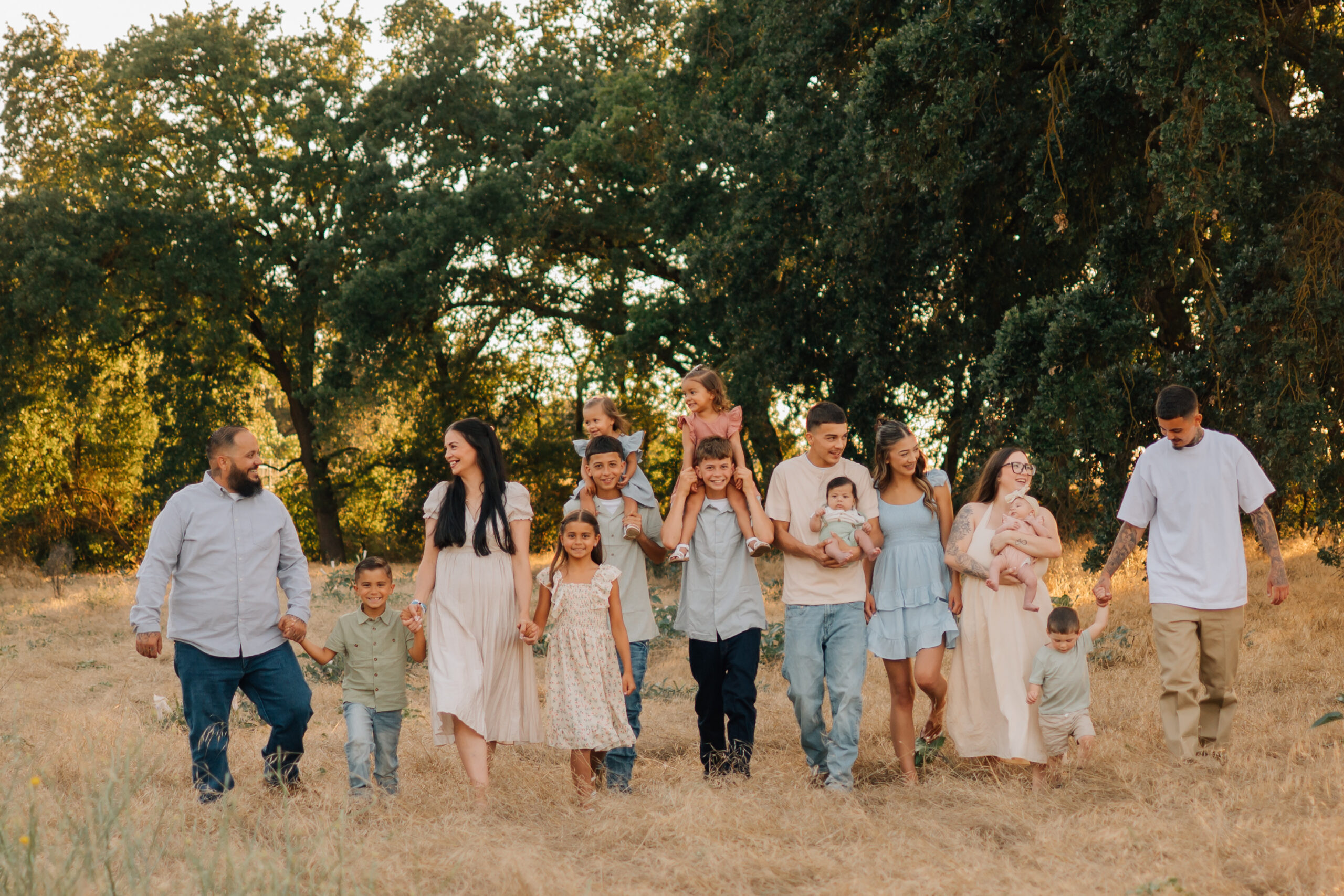 Young children riding on their older siblings’ shoulders while the family laughs together outdoors.