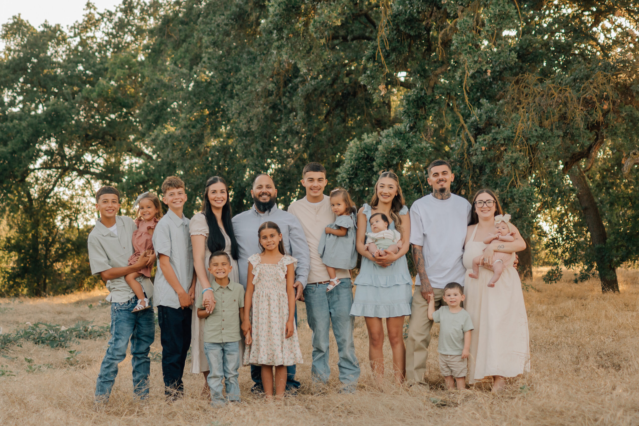 Extended family of 15 smiling together during a golden-hour photo session at Oak Grove Park in Ripon, California.