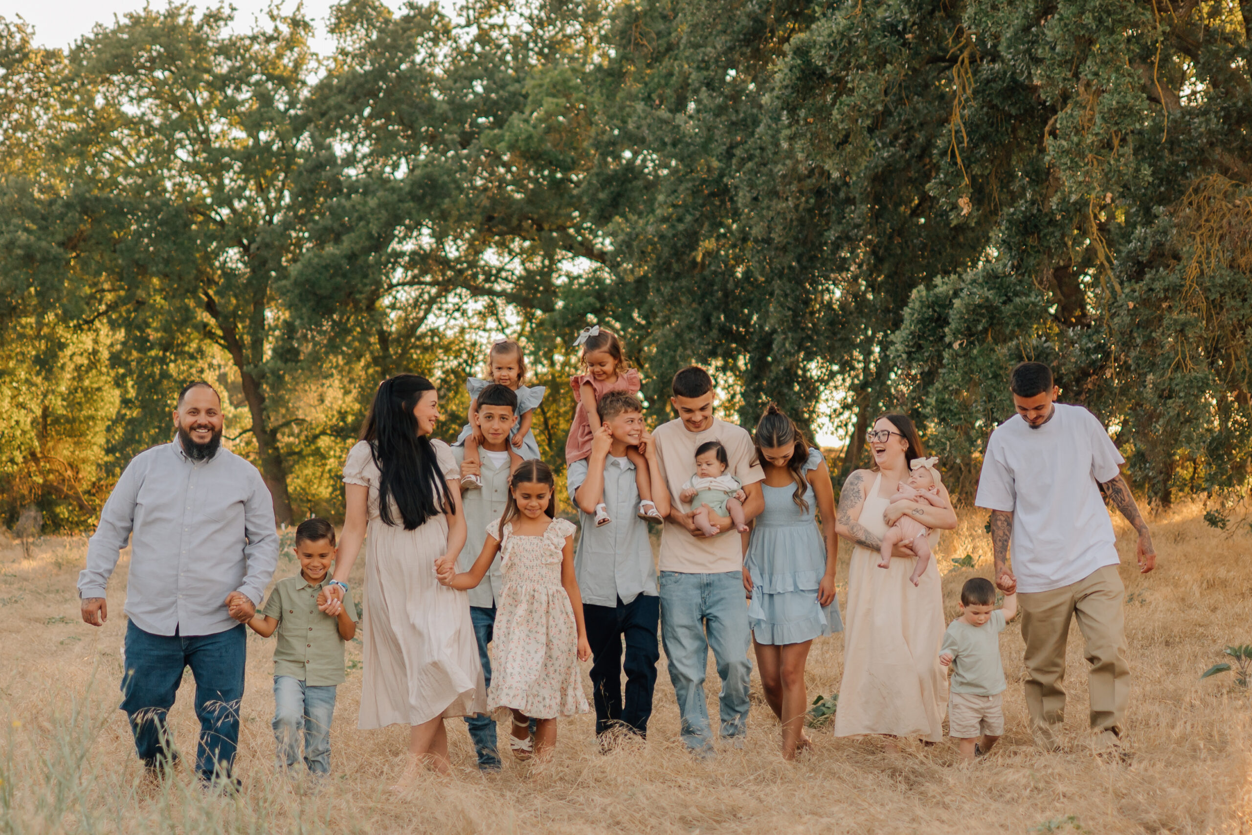Extended family walking hand in hand through dry golden grass during a summer family photography session in Ripon.