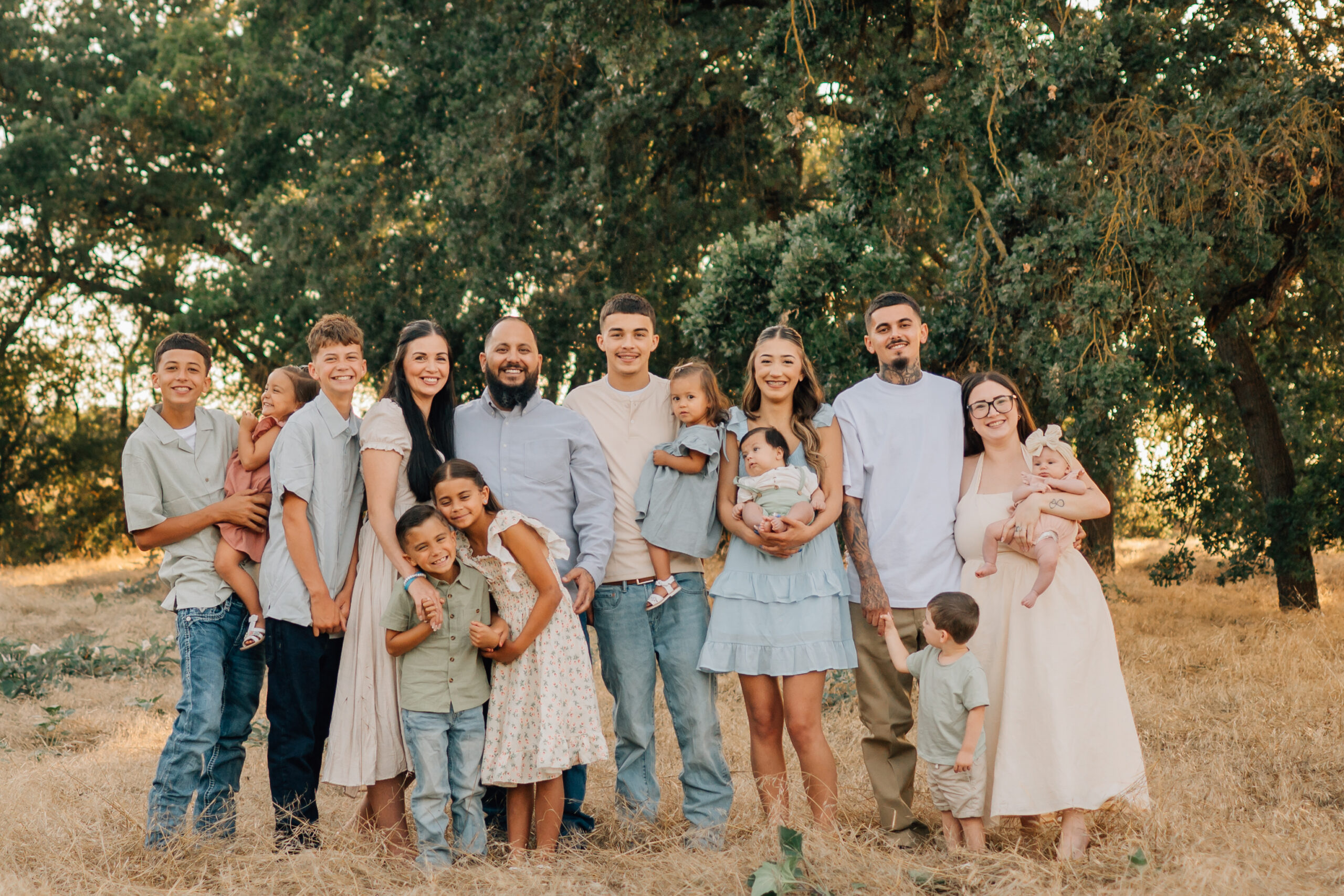 Extended family of 15 smiling together during a golden-hour photo session at Oak Grove Park in Ripon, California.