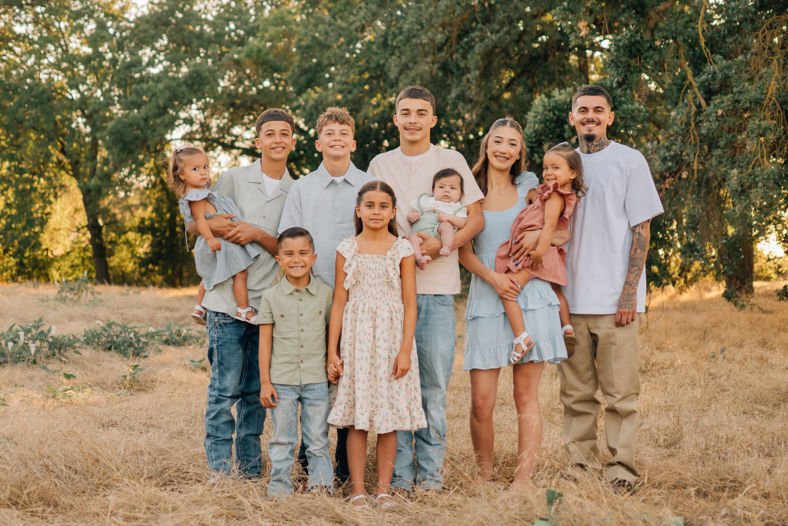 Brothers and sisters smiling together with younger siblings and babies during an outdoor family session.