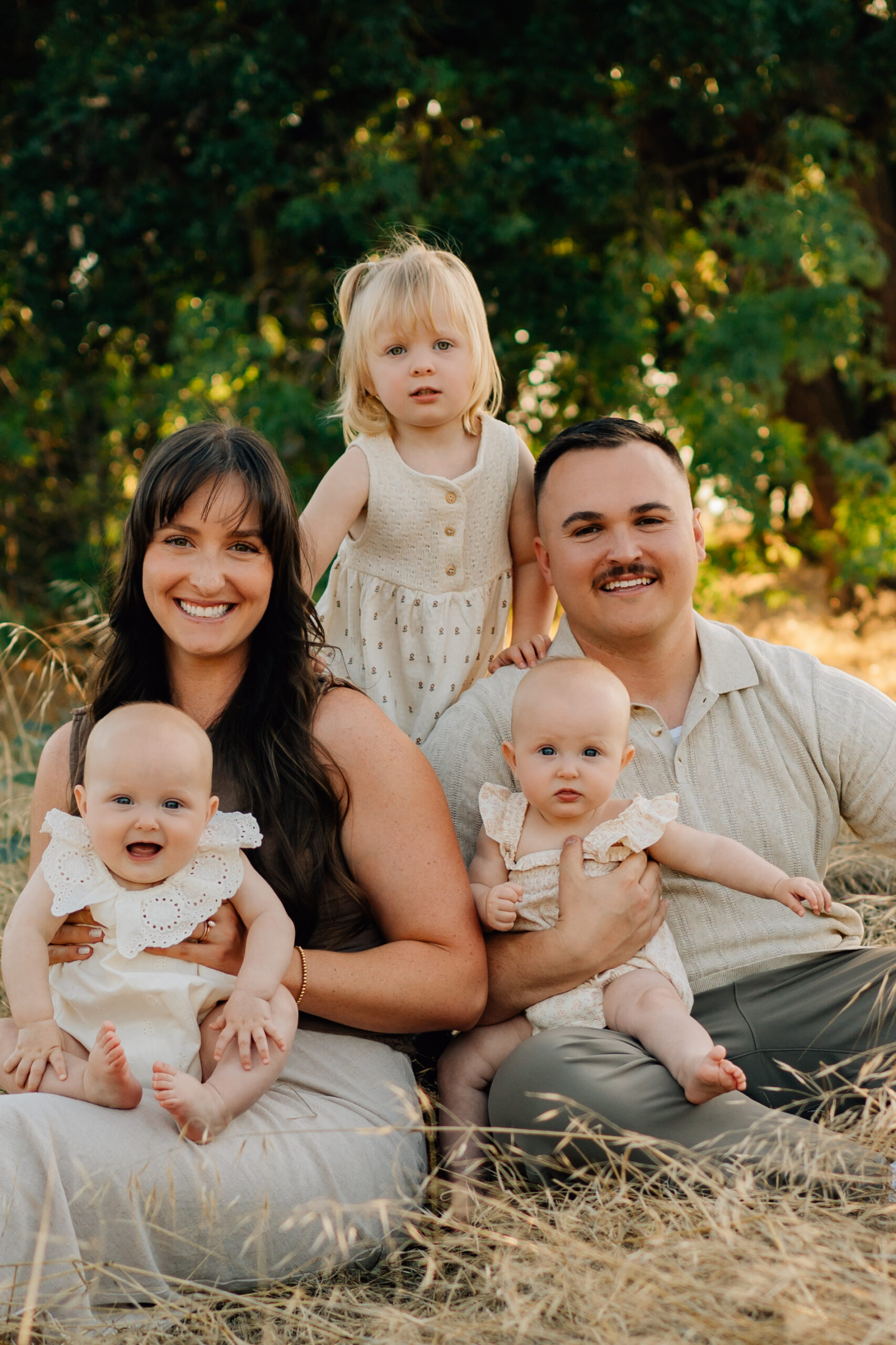 Family of five sitting together in a grassy field during a relaxed outdoor family session at Oak Grove Park.