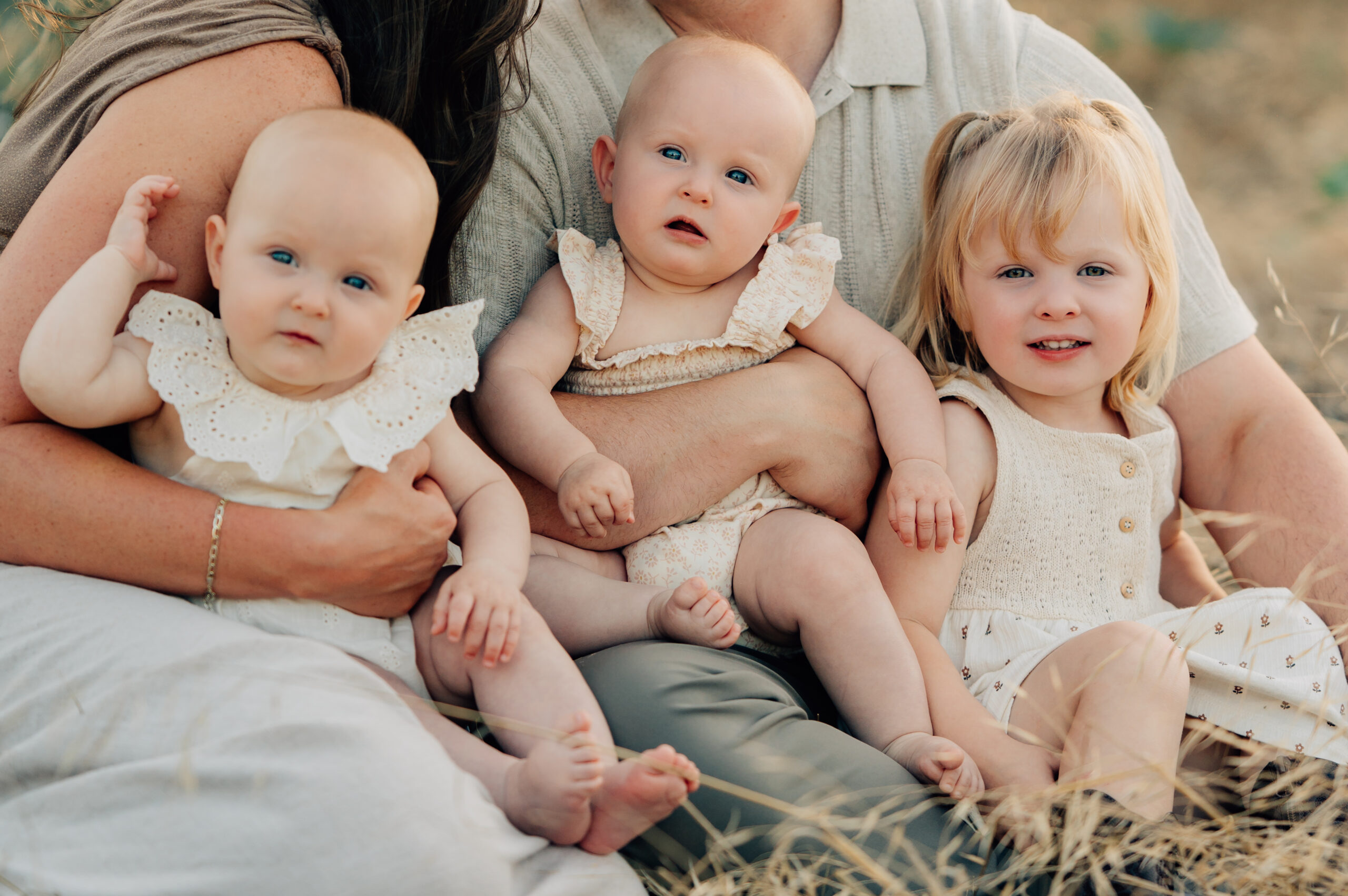Siblings looking at the camera as they sit in their parents laps.