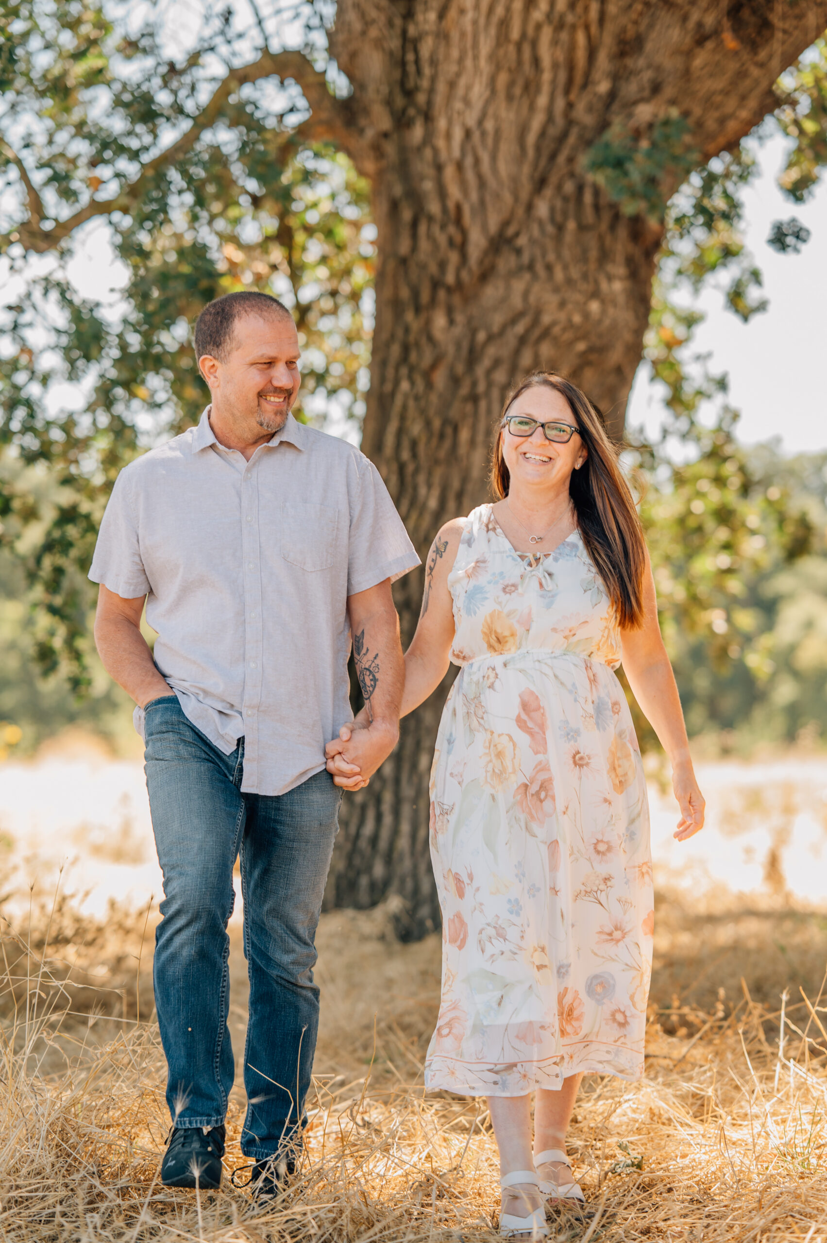 A couple walking towards the camera under an oak tree. 